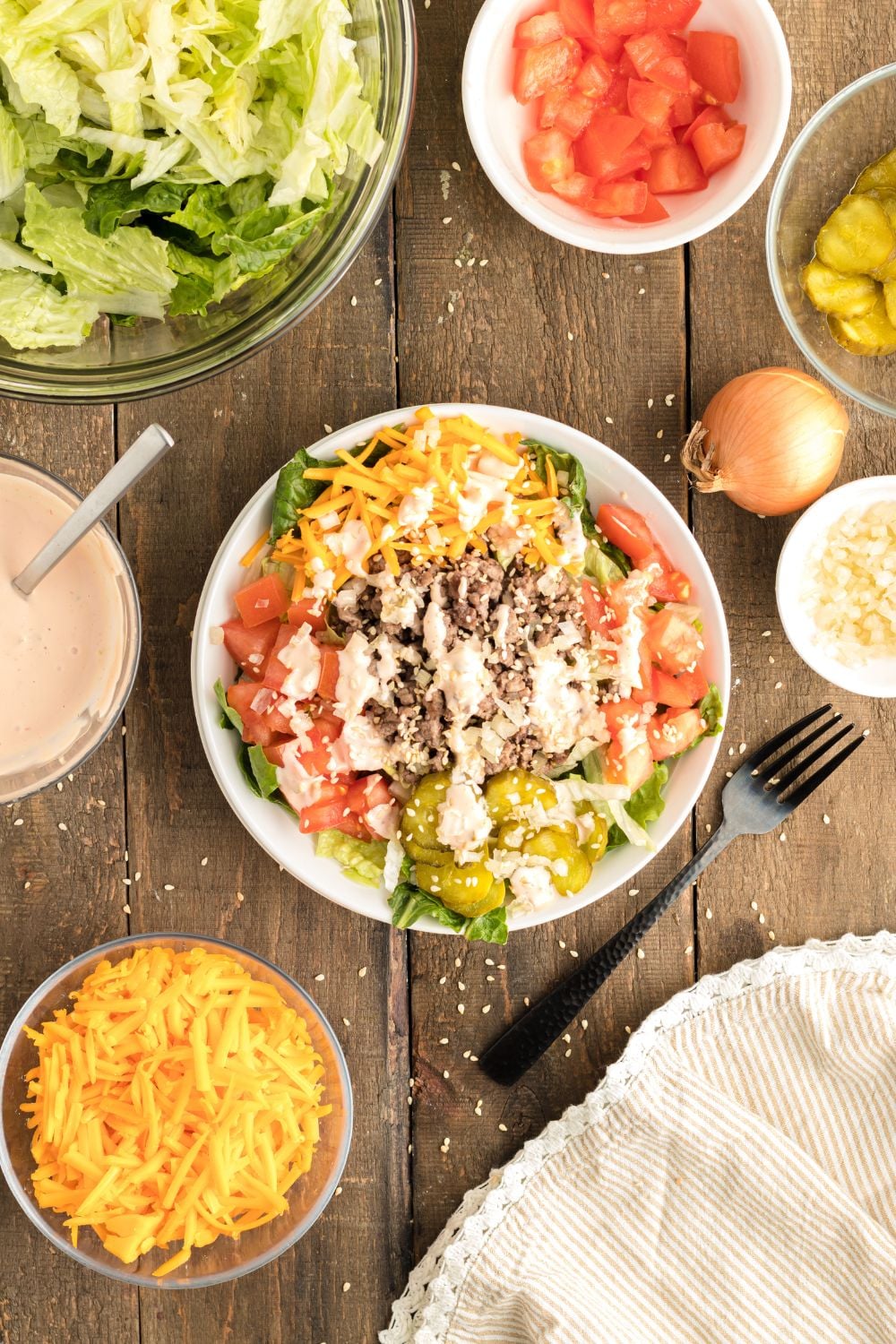 Big Mac Salad in a bowl with ingredients in separate bowls all around it on the wooden table 