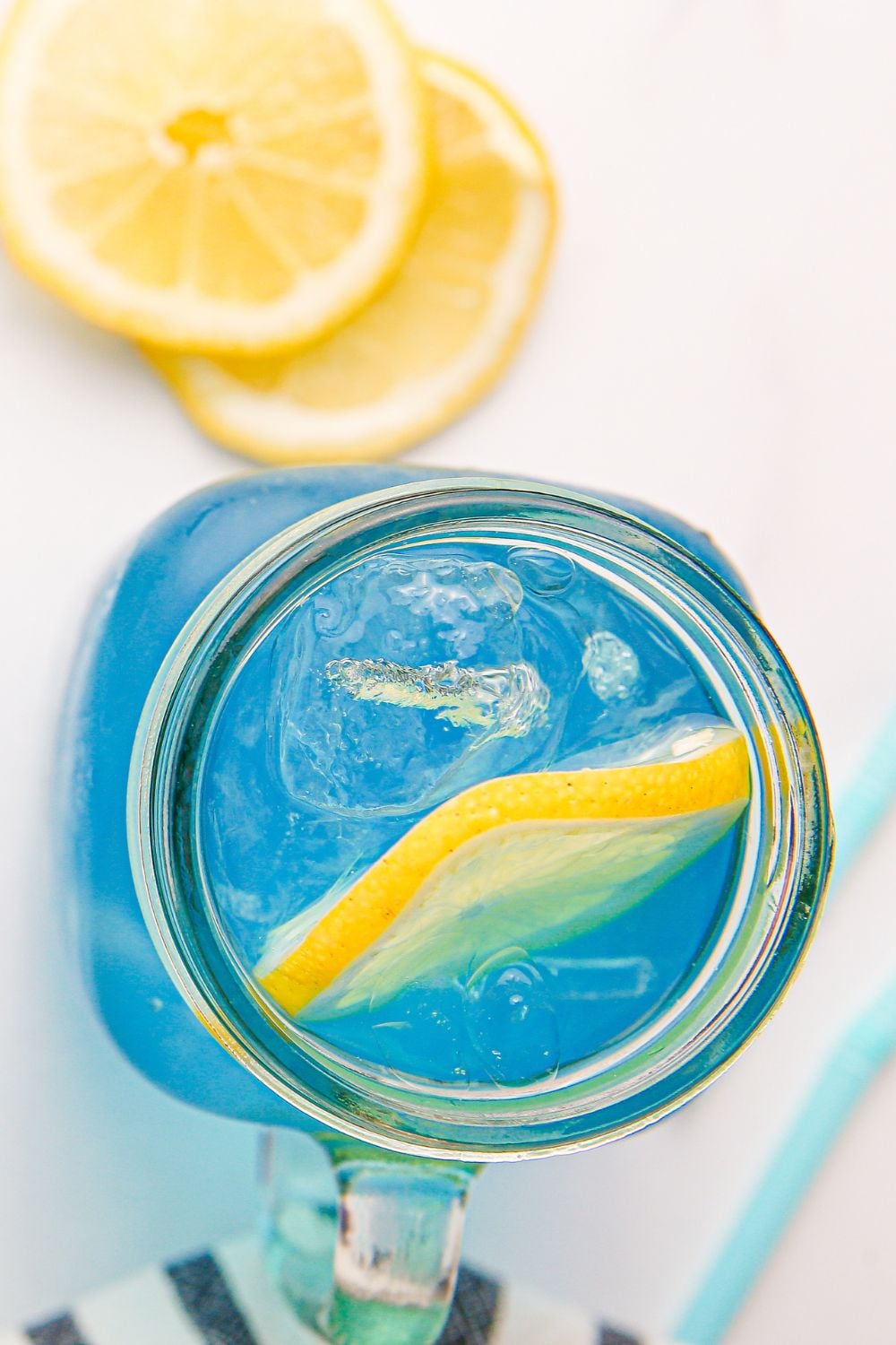 overhead look of glass with Blue Raspberry Lemonade in it and a few lemon slices on table