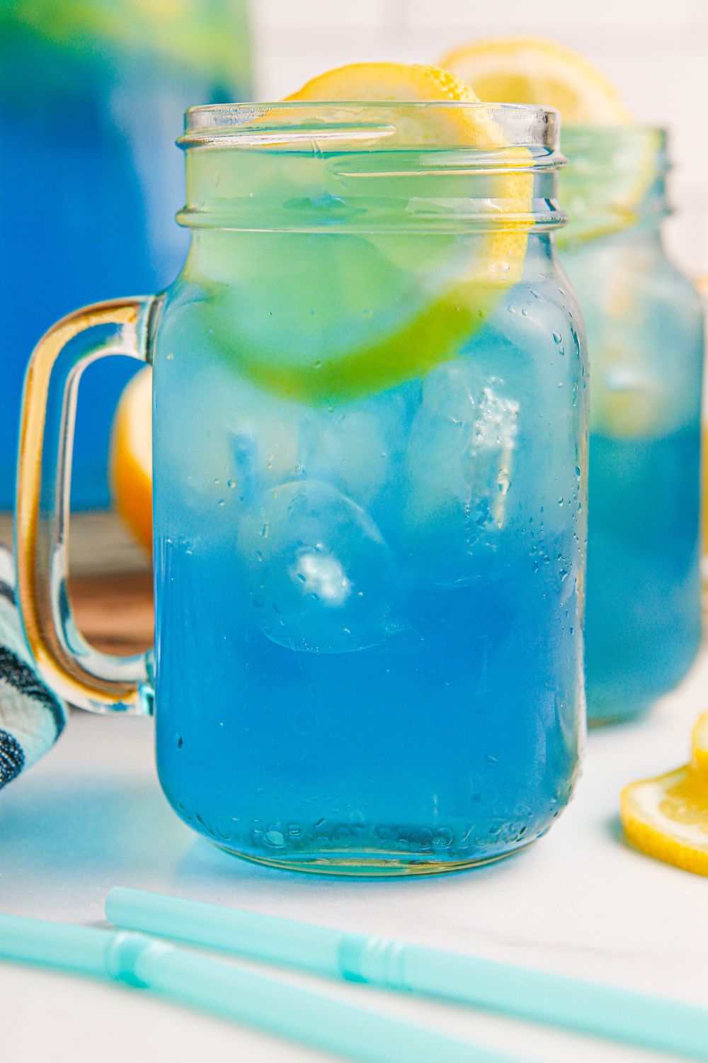 close up of Blue Raspberry Lemonade in mason jars on table with a few straws in front