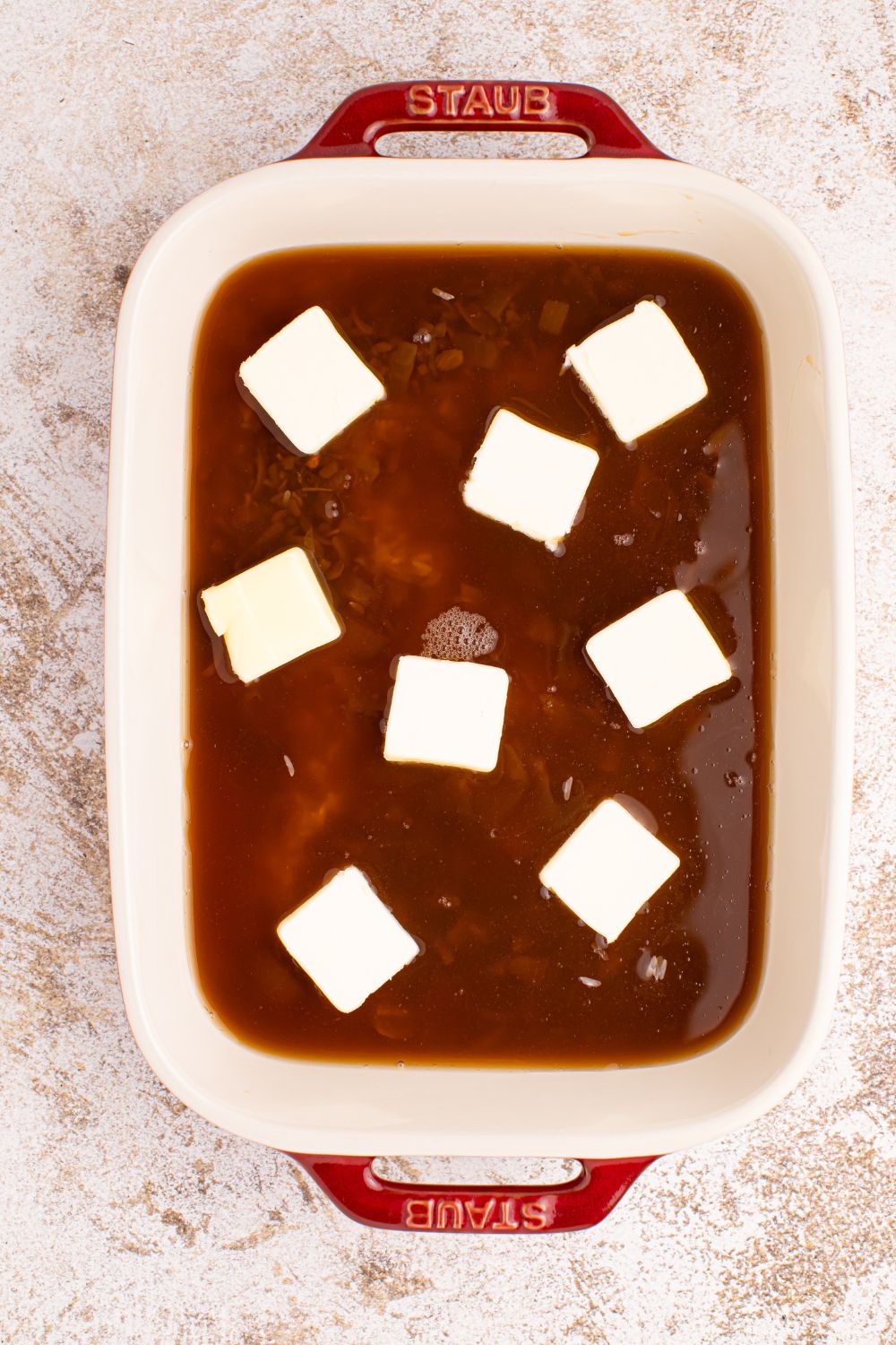 Stick of Butter Rice mixture in a casserole dish with slabs of butter on top
