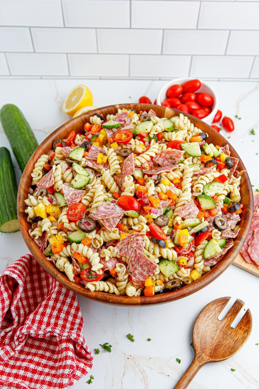 Summer Pasta Salad in a wooden bowl on table with vegetables around it 
