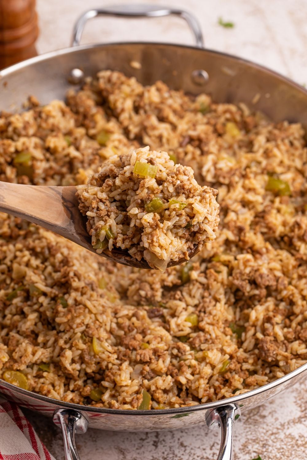 Dirty Rice in a pan with a scoop on a wooden spoon above the pan