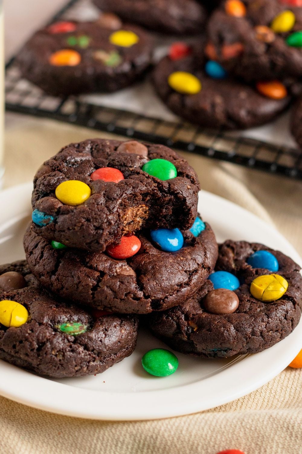 Chocolate M&M Cookies stacked on a white plate on table with a cookie with a bite taken out of it