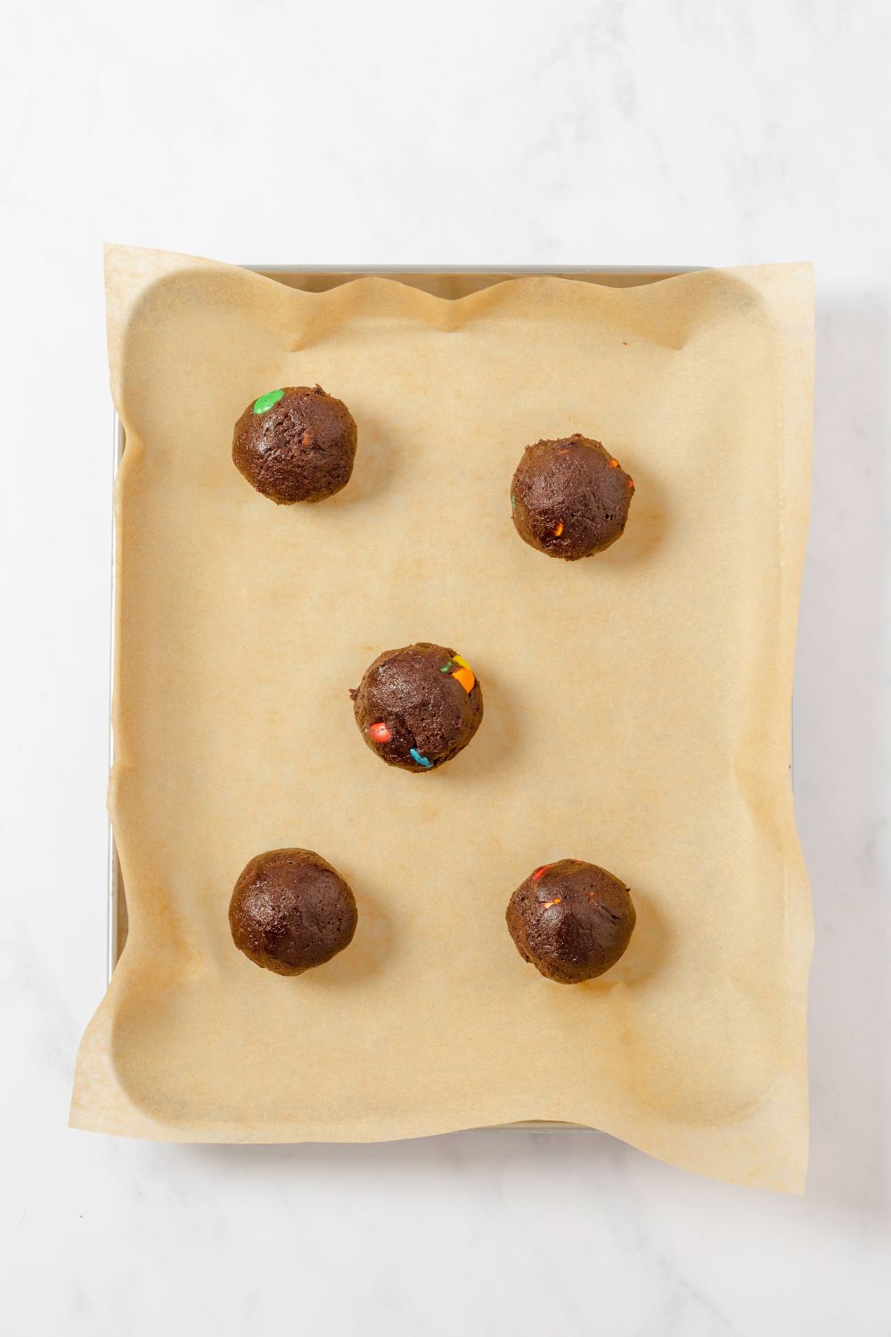 Chocolate M&M Cookie dough balls on a lined cookie sheet