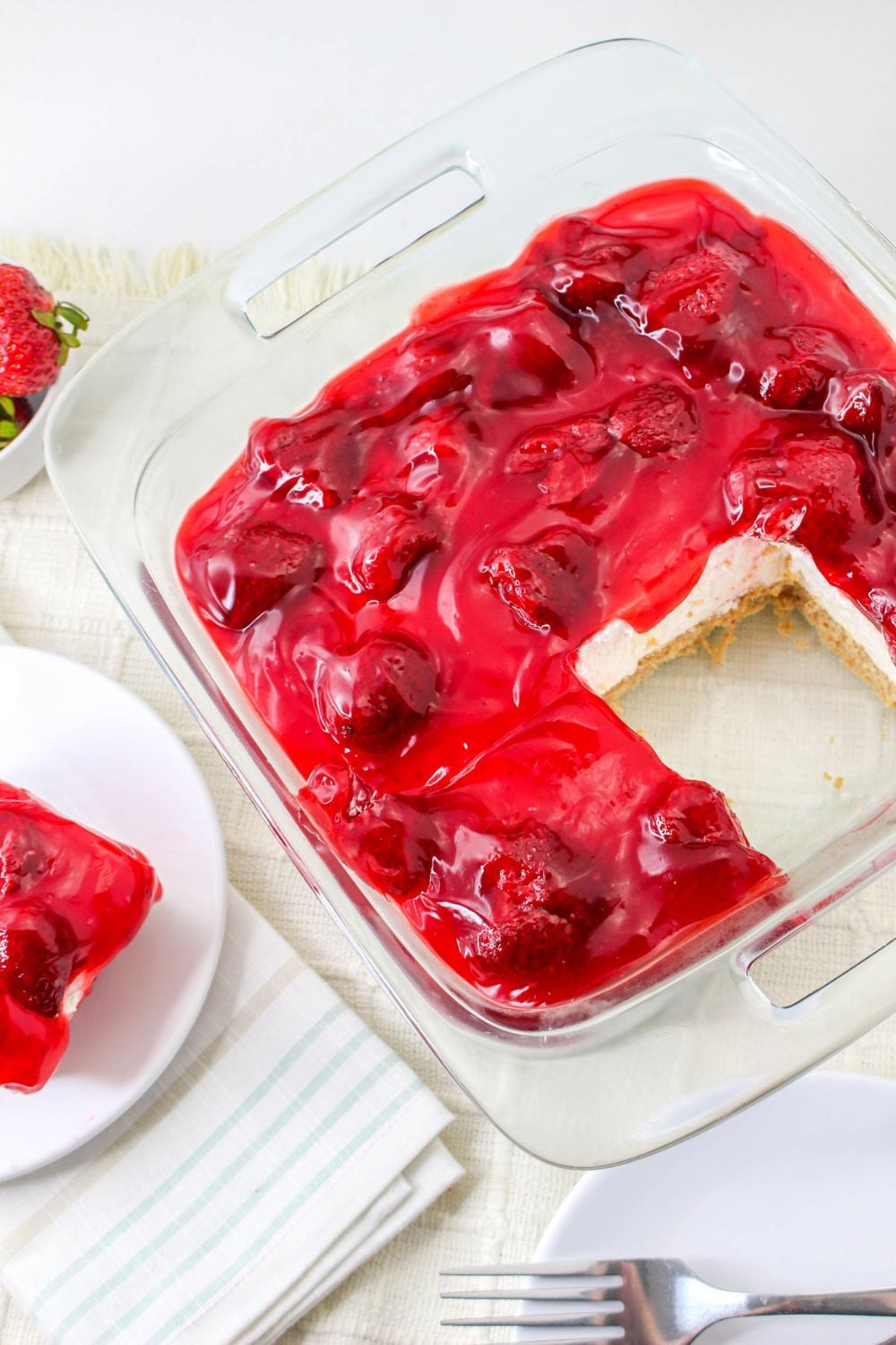 overhead look of No Bake Strawberry Delight on table with a slice taken out and a small plate with dessert on it