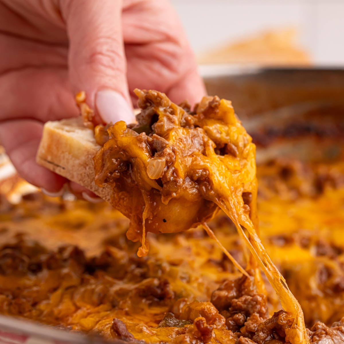 Sloppy Joe Dip in pan with a piece of bread and dip being lifted out of pan with hand