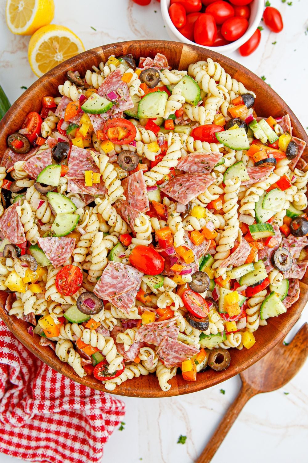 Summer Pasta Salad in a bowl with spoon beside it and tomatoes and lemons on the side of bowl 