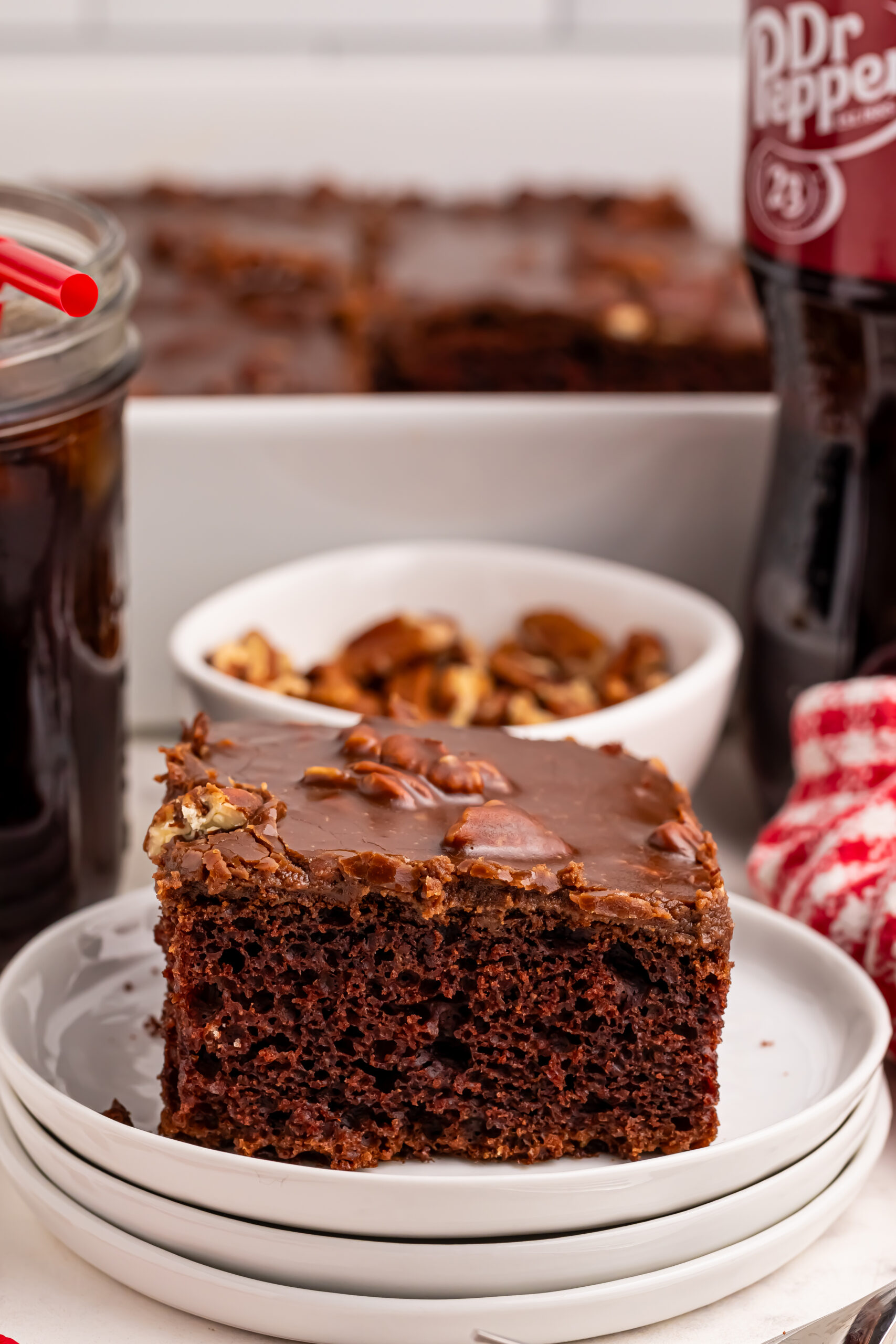 Dr. Pepper Cake slice of cake on plate with a bowl of walnuts behind it on table