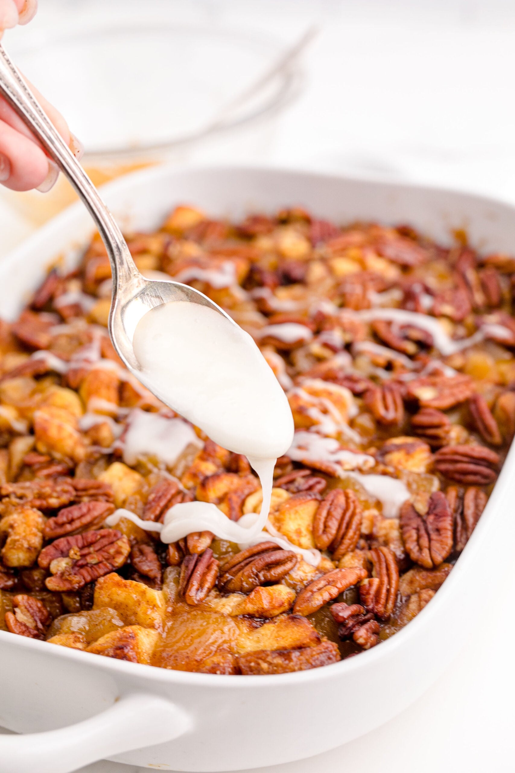 Cinnamon Roll Casserole in a white baking dish with a spoon drizzling icing on top