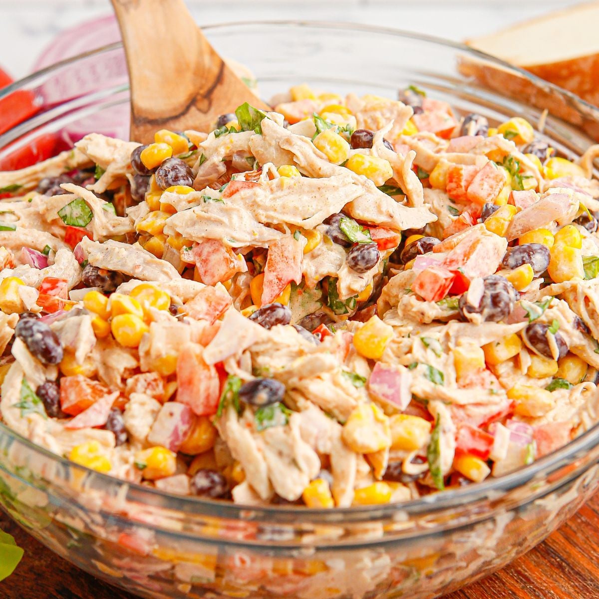 Southwest Chicken Salad in a glass bowl sitting on table with a wooden spoon in the bowl