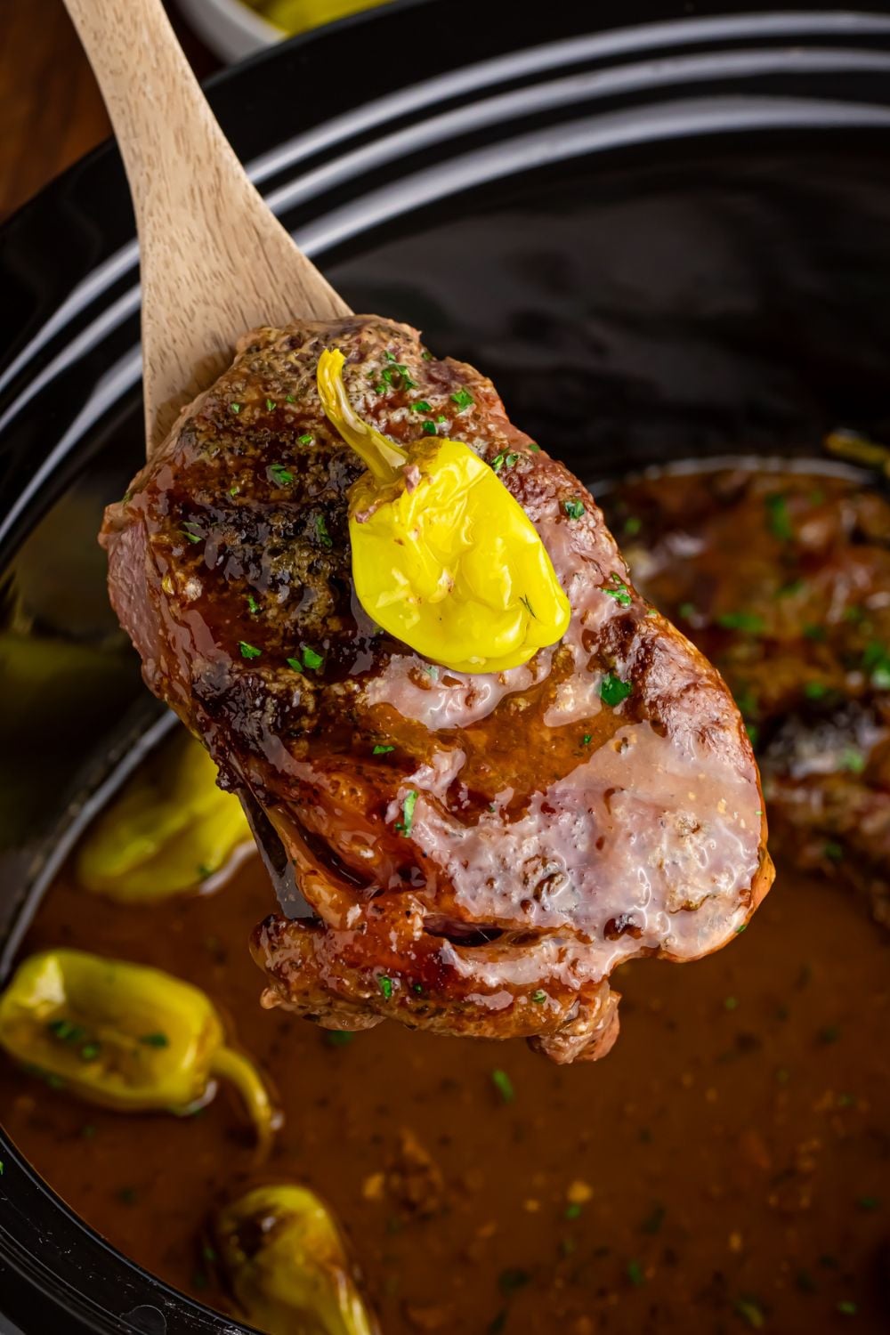 steak being lifted out of slow cooker with spoon - Slow Cooker Mississippi Ribeye Steaks