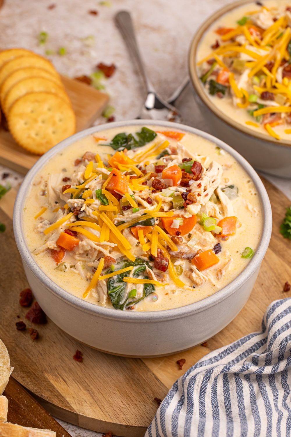 soup in bowls on table with a spoon in bowl and crackers behind it on table