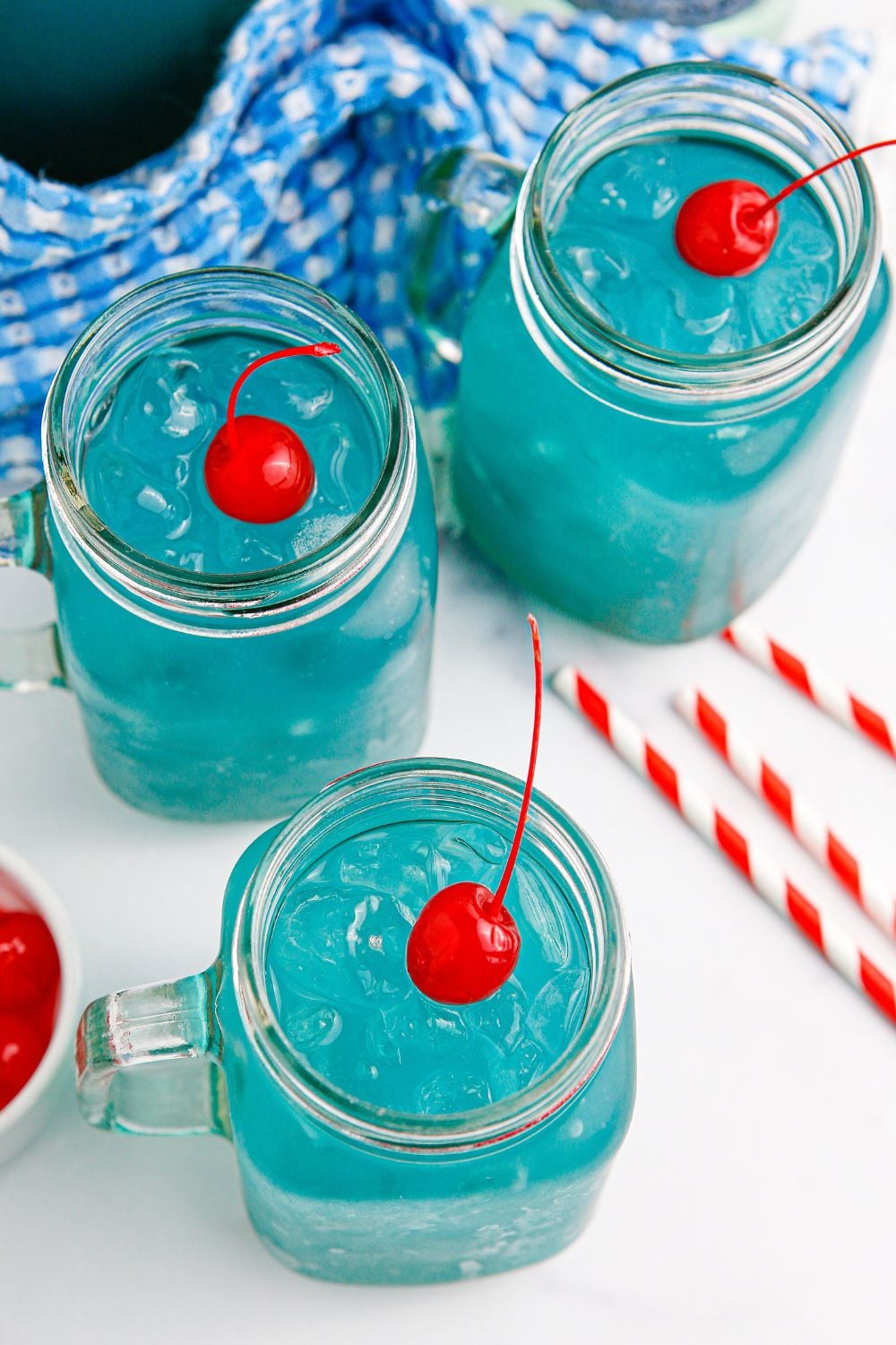 blue drinks in glasses with a red cherry on top of each glass