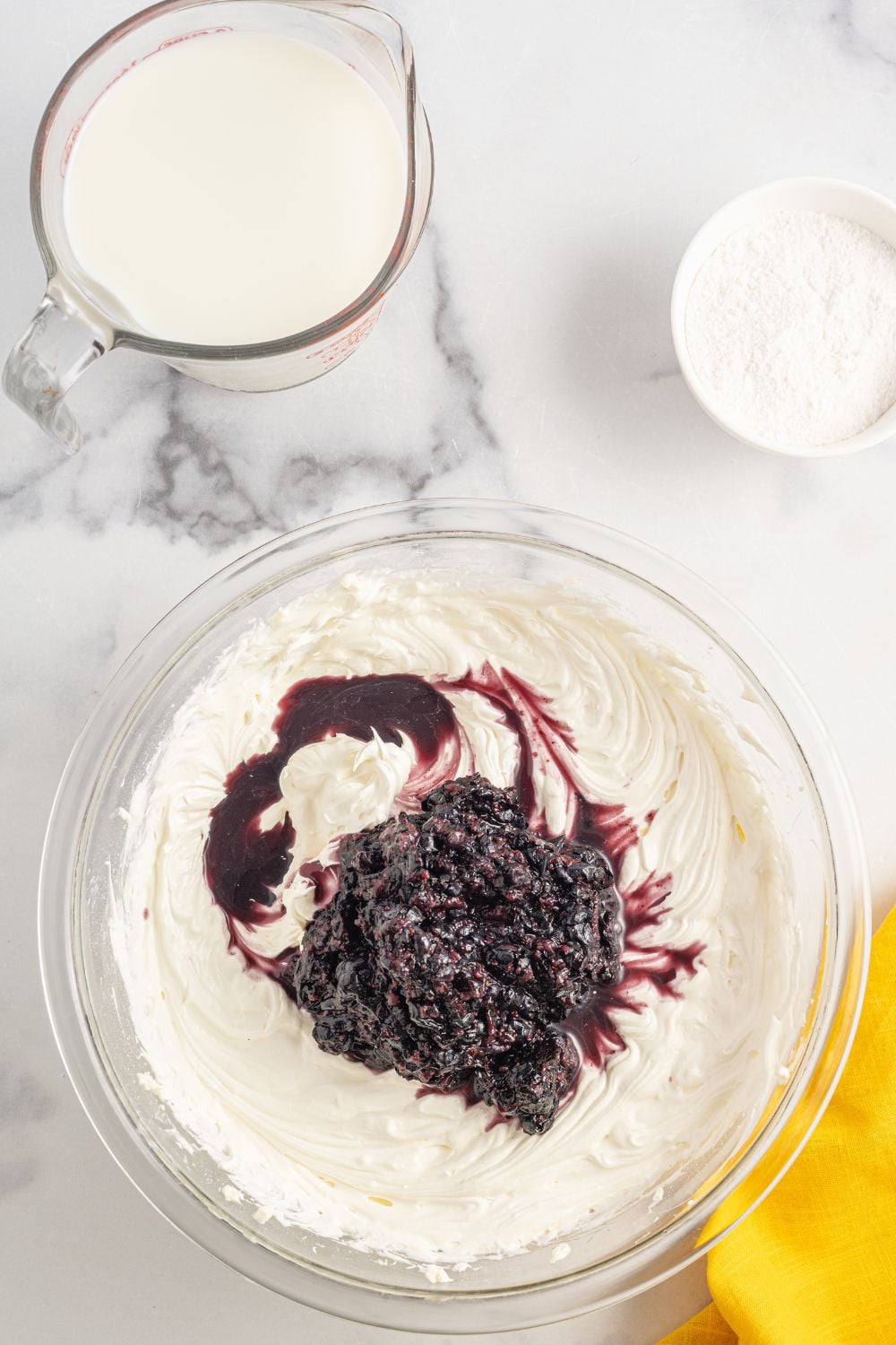 Cream cheese and blueberry mixure in a bowl sitting on the table with other ingredients around it