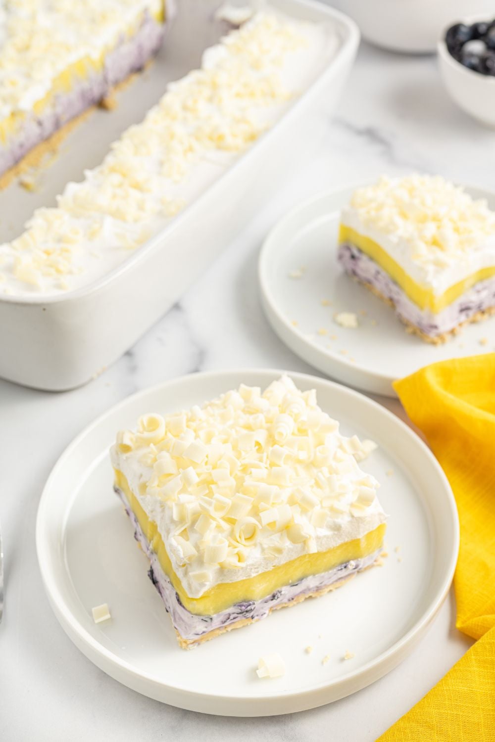 blueberry lemon lasagna sliced on plates with the dish behind it