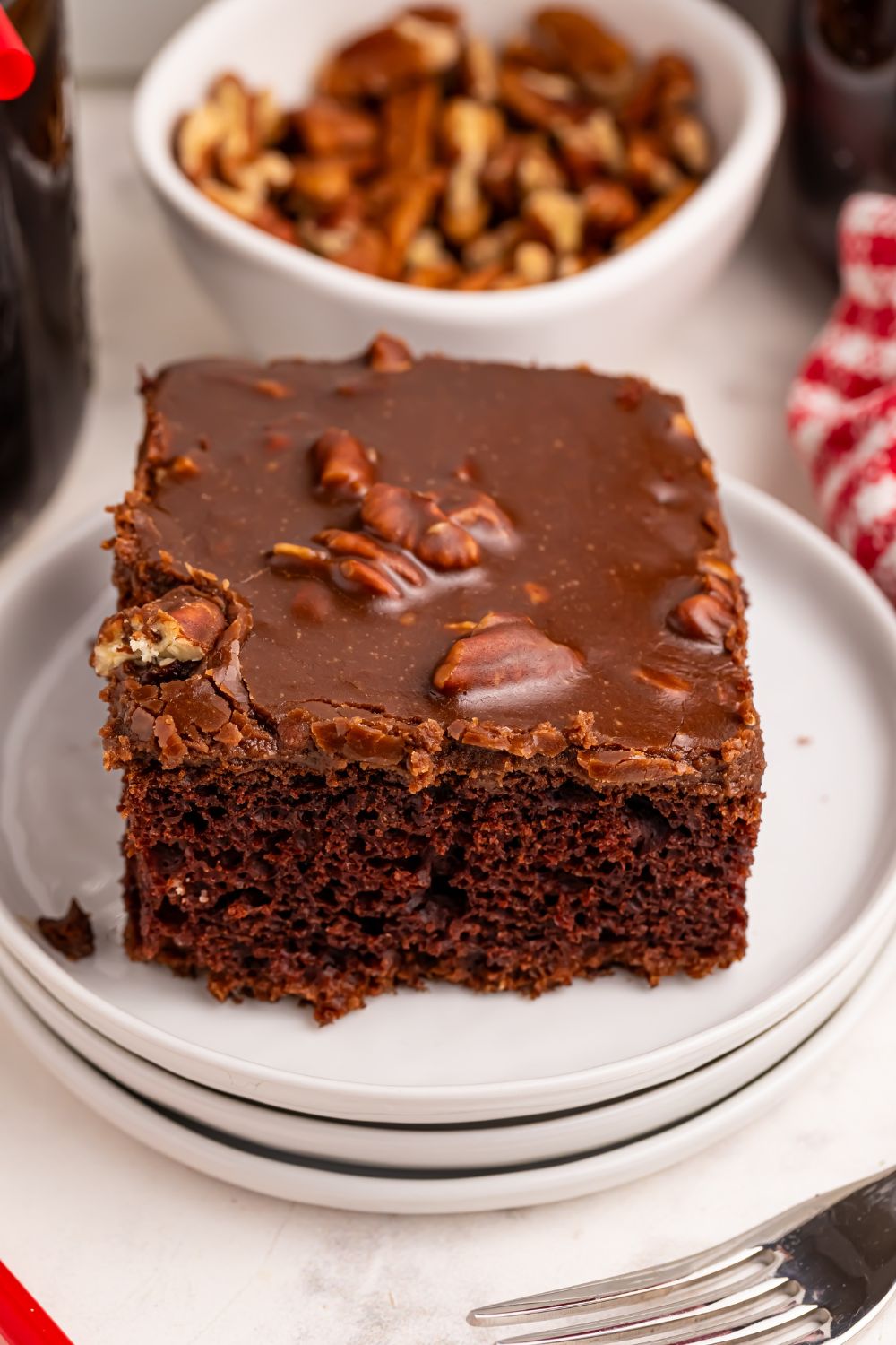Dr. Pepper Cake slice of cake on plate with a bowl of walnuts behind it on table