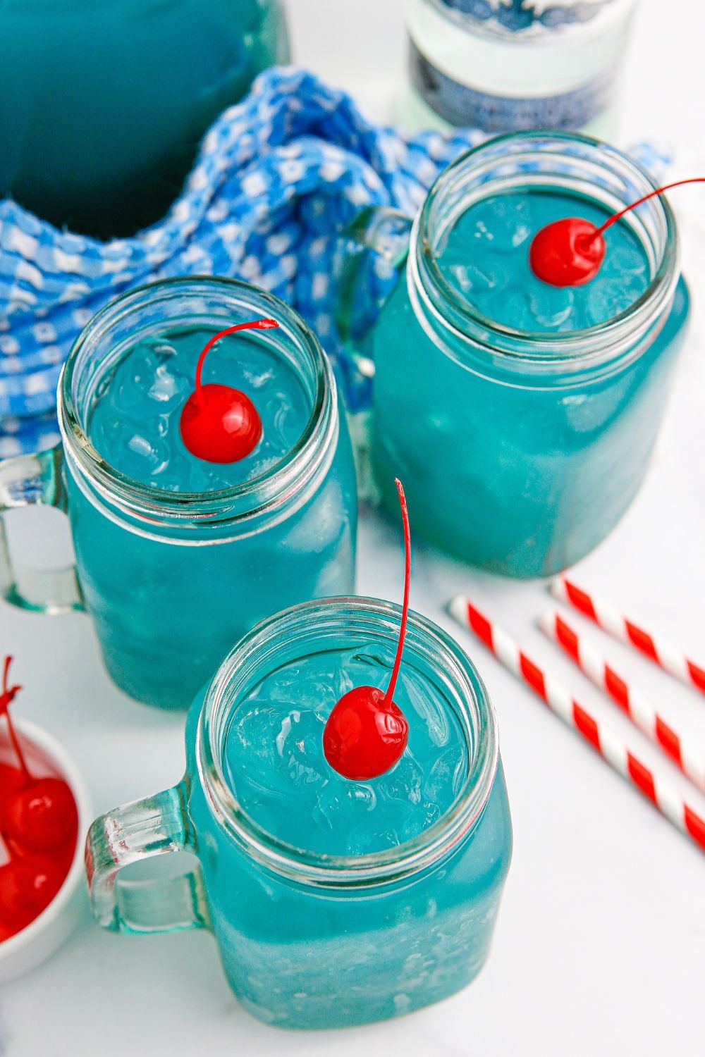 glasses of blue cocktails with a cherry on the top of the ice in each glass