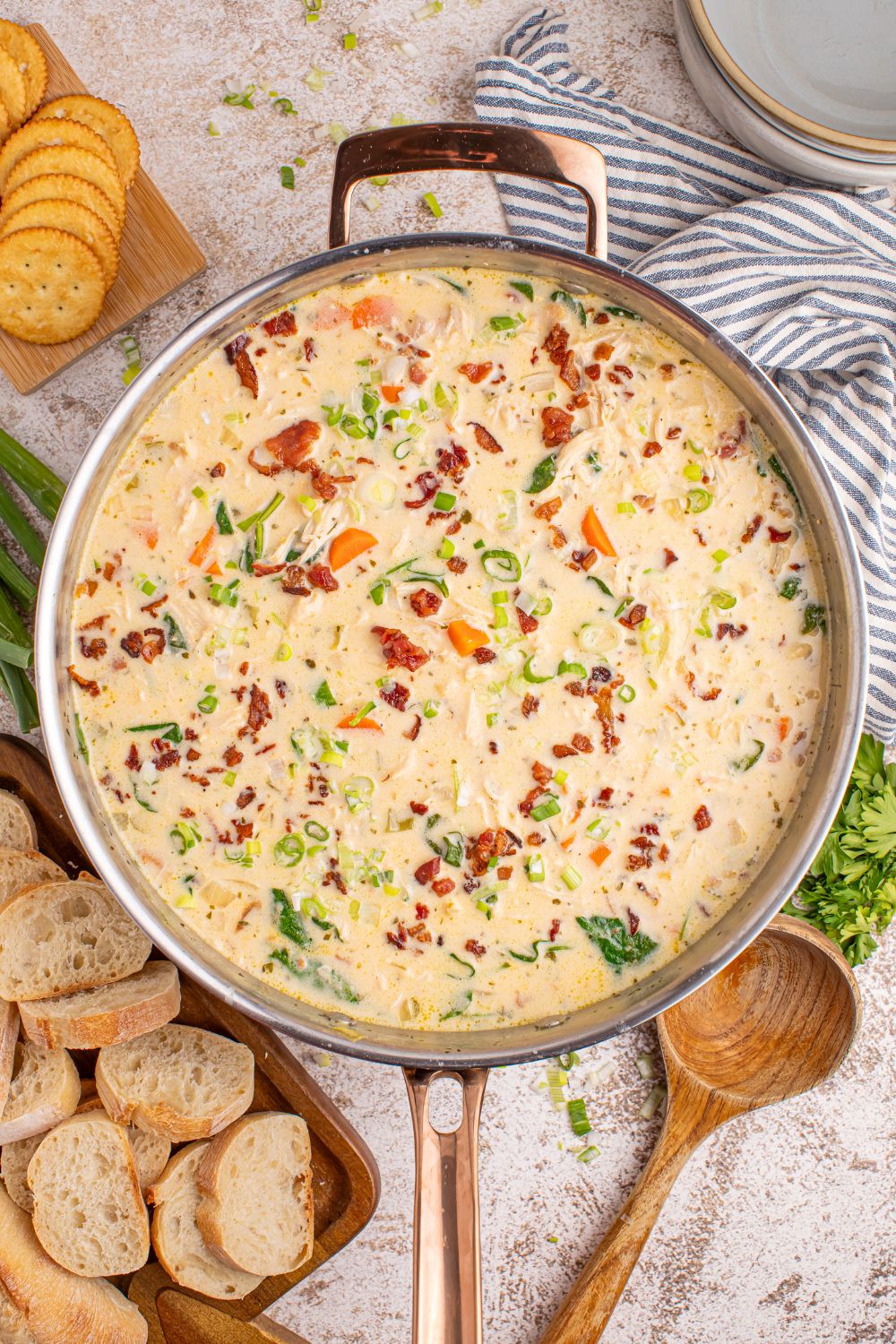 overhead look of Crack Chicken Soup in a pan on table with sliced bread around it, herbs and a wooden spoon
