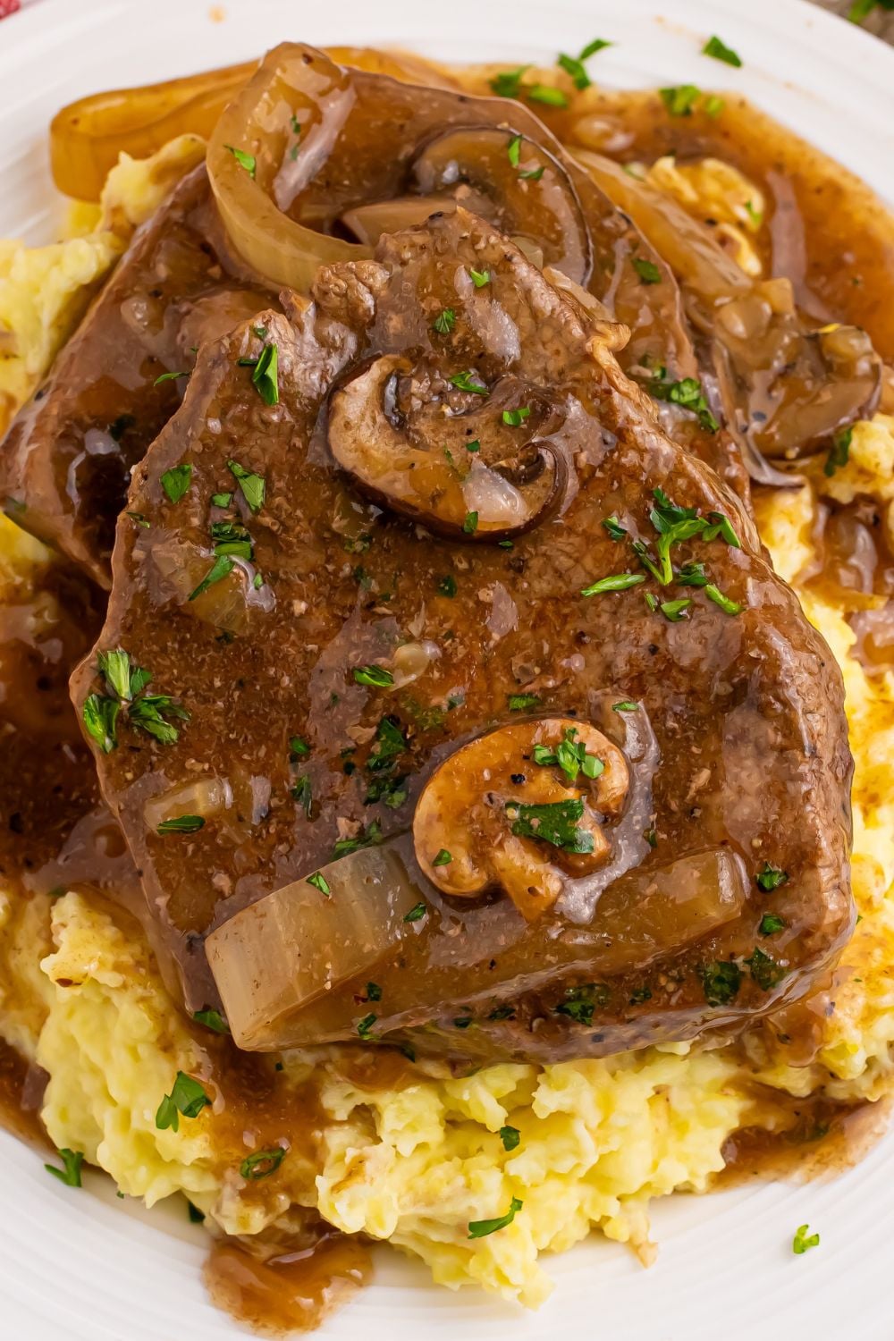 Slow Cooker Round Steak and Gravy on a plat with mashed potatoes under the steak