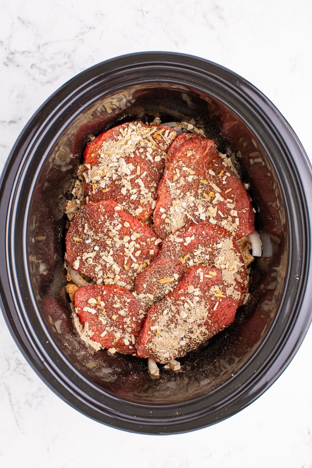 slow cooker with round steak topped with an onion soup mix spread over the meat
