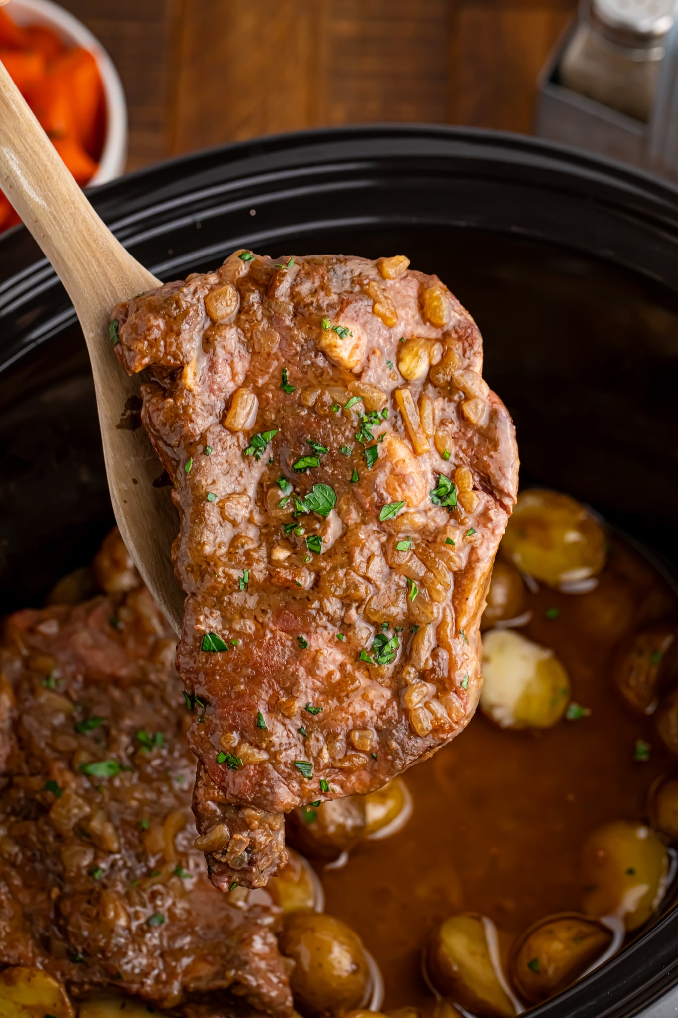 Crock Pot Steak being lifted out of the crock pot with a wooden spoon