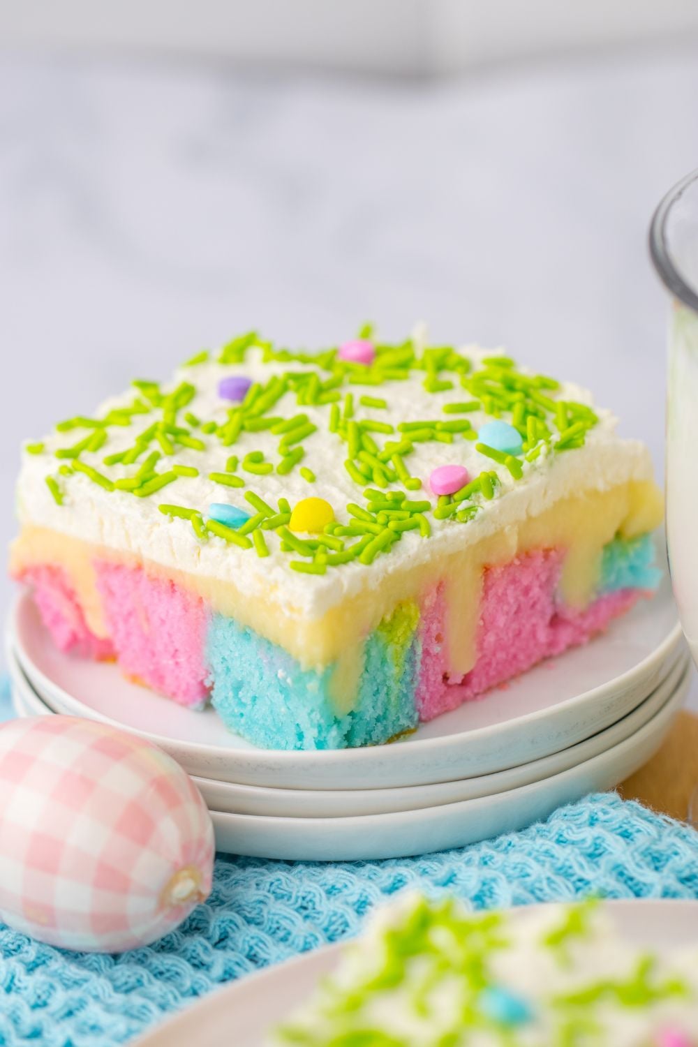 stacked plates with a slice of the Easter Poke Cake on top with Easter eggs around it on table