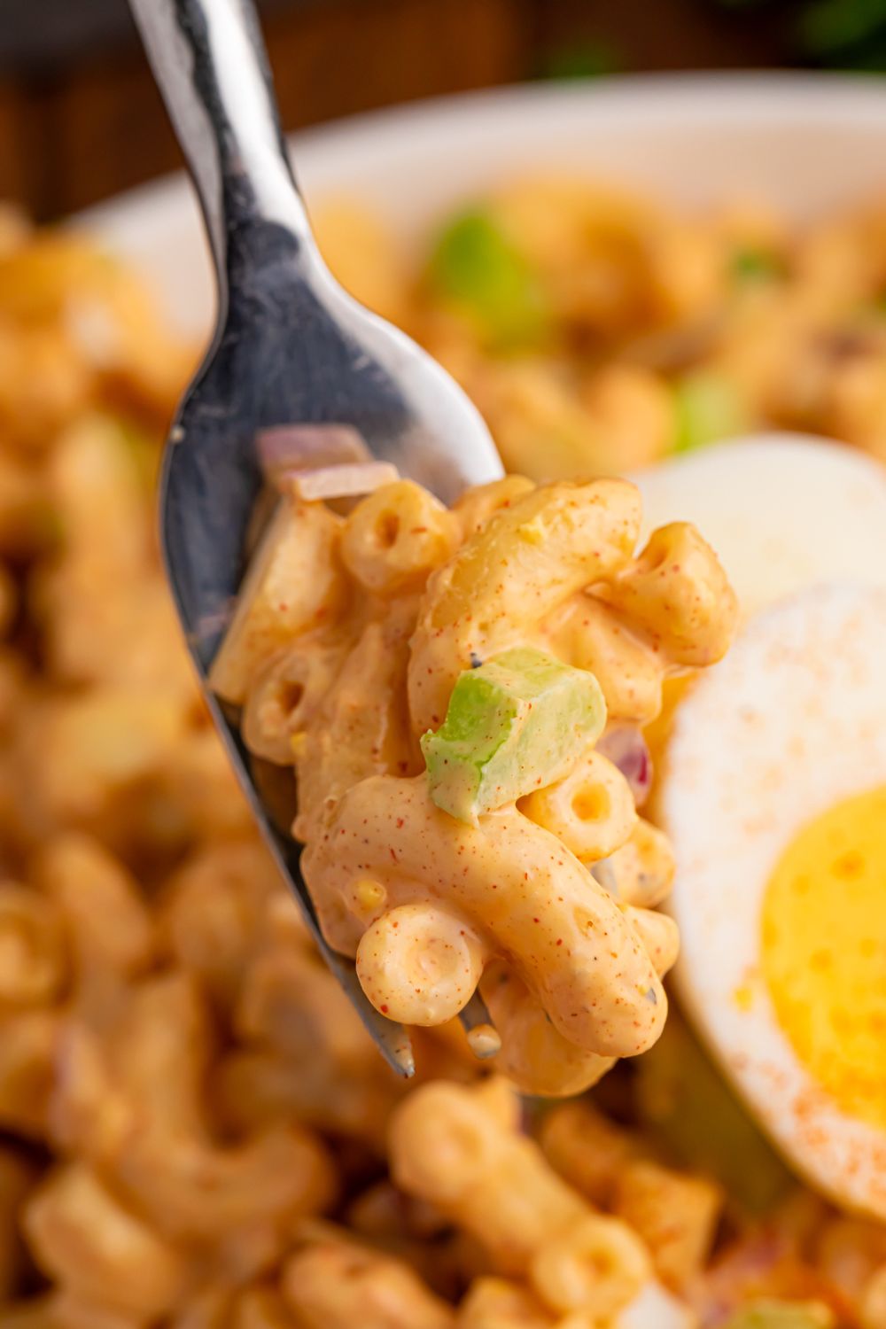 Deviled Egg Pasta Salad on a fork above a plate with pasta salad on it