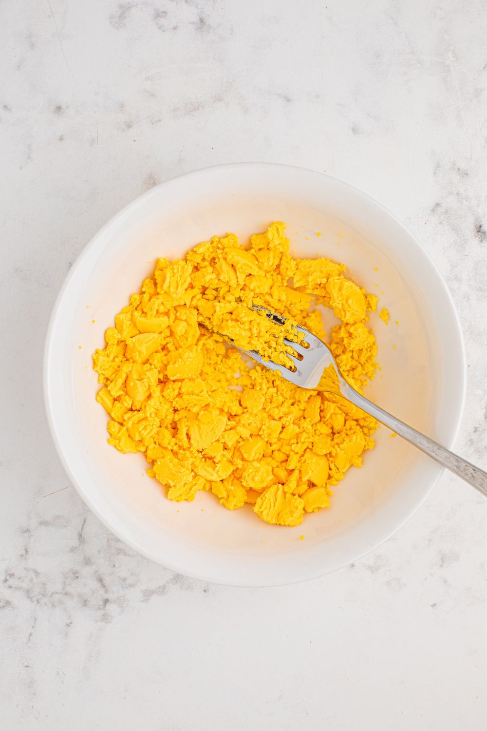 hard boiled egg yolks mashed up with a fork in a bowl to make a crumbled texture