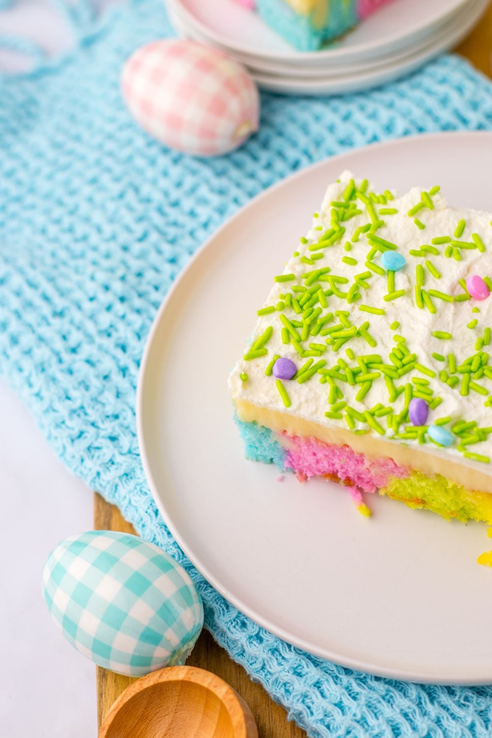 slice of Easter Poke Cake on a plate with fabric eggs around it on the table