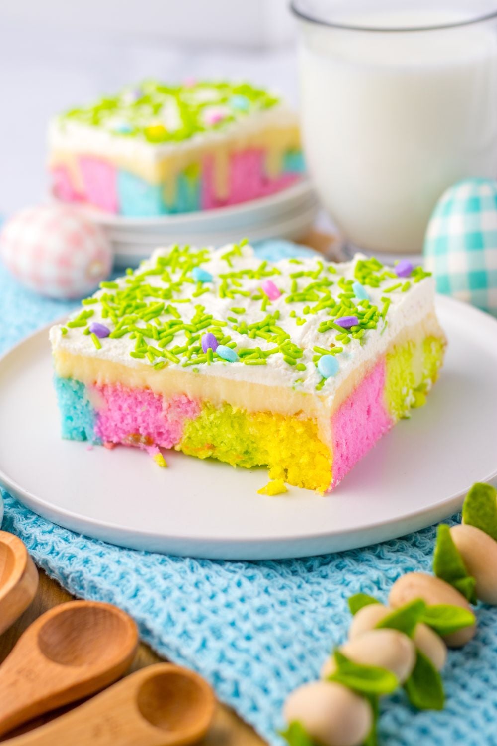 slices of Easter Poke Cake on plates on table with a glass of milk set to the side