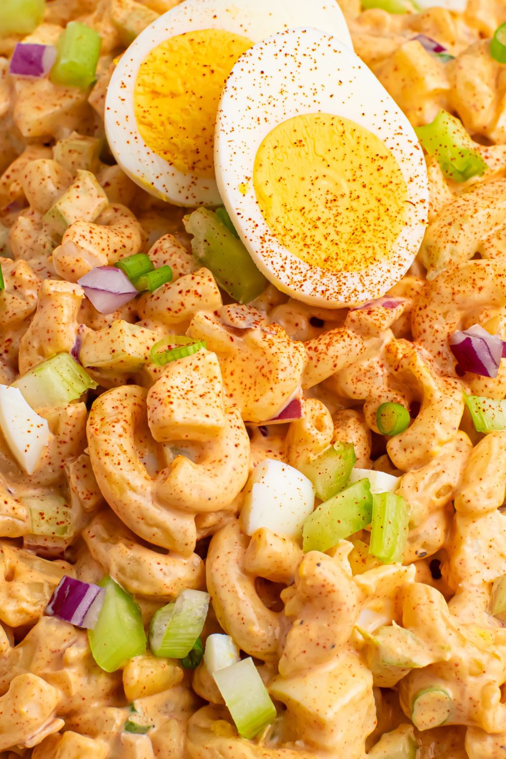 Deviled Egg Pasta Salad in a bowl with a hard boiled egg on top with paprika sprinkled on top