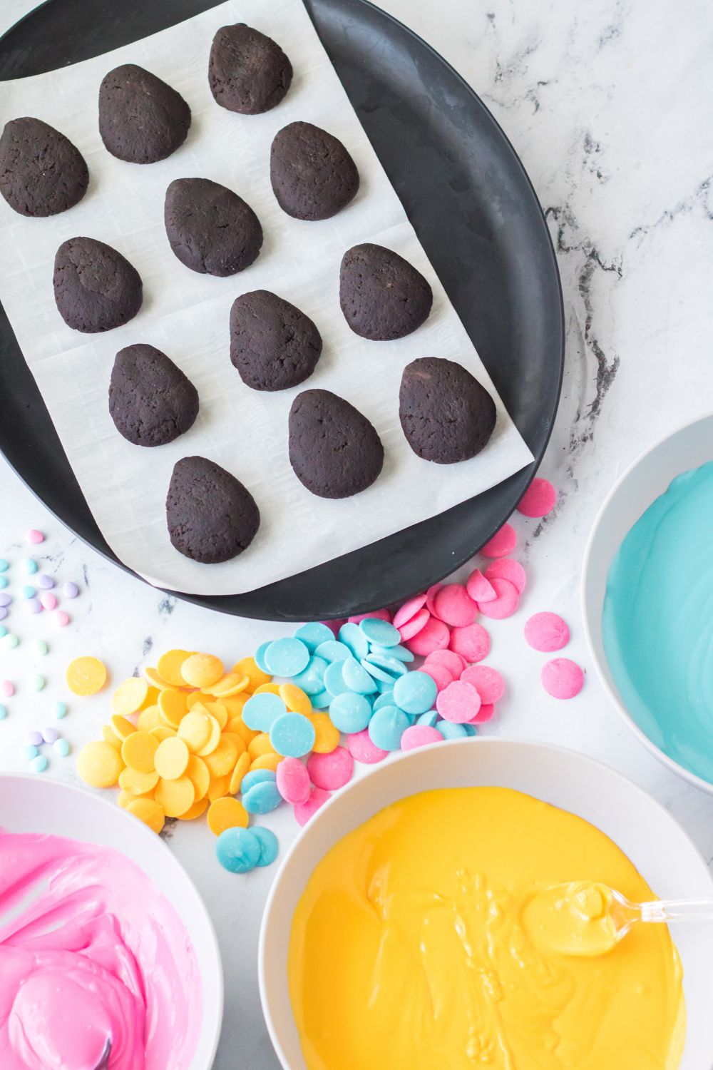 egg shaped Easter Egg Oreo Truffles on table with melted chocolates in bowls