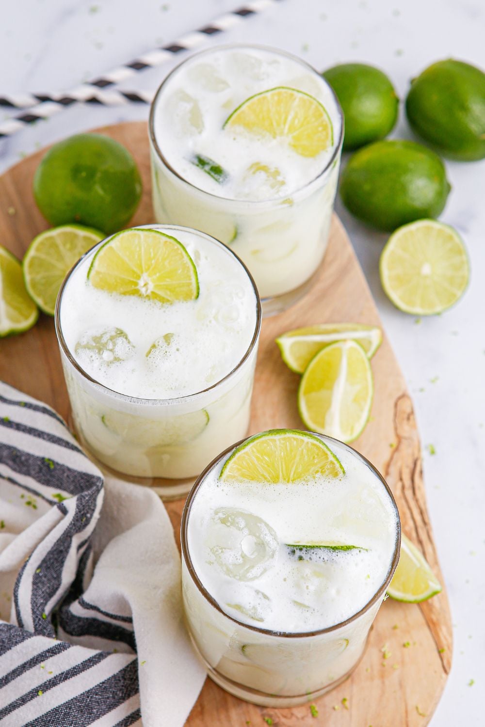 limeades in glasses on table with blue and white towel and limes placed around glasses