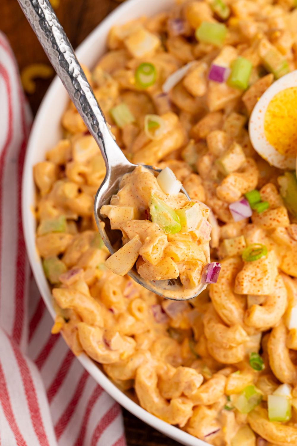 spoon with deviled egg pasta salad in it with a bowl full of it under