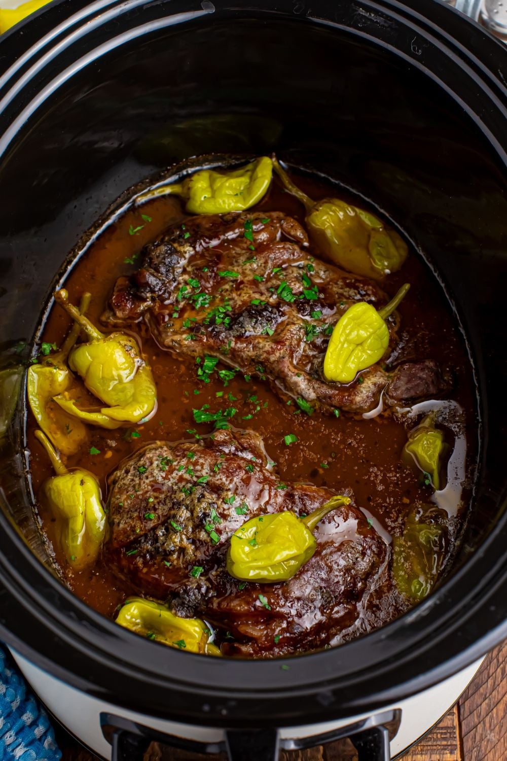Slow Cooker Mississippi Ribeye Steaks sitting in a crockpot wih peppers on top