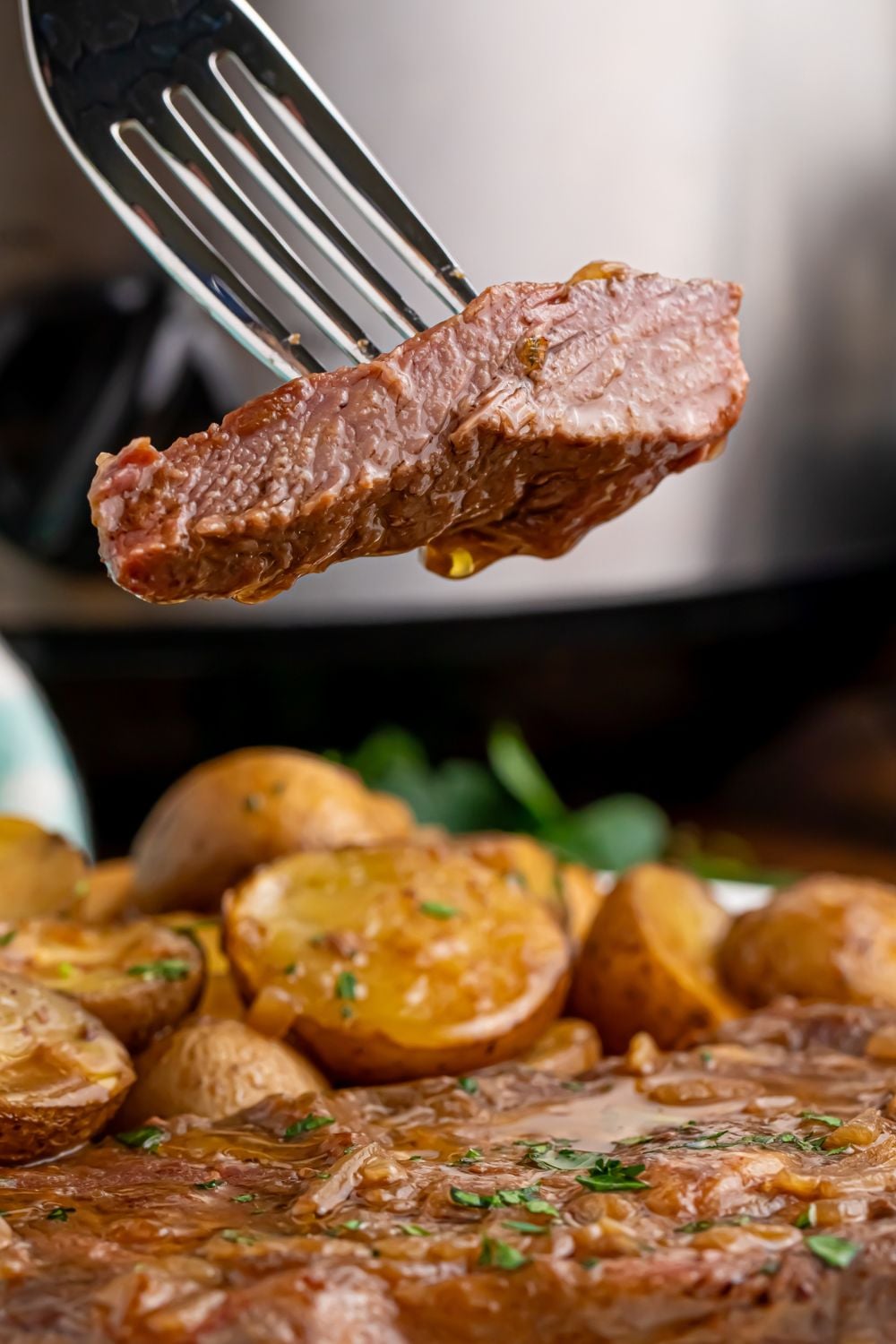 slice of steak on fork with a plate full of Crock Pot Steak and Potatoes