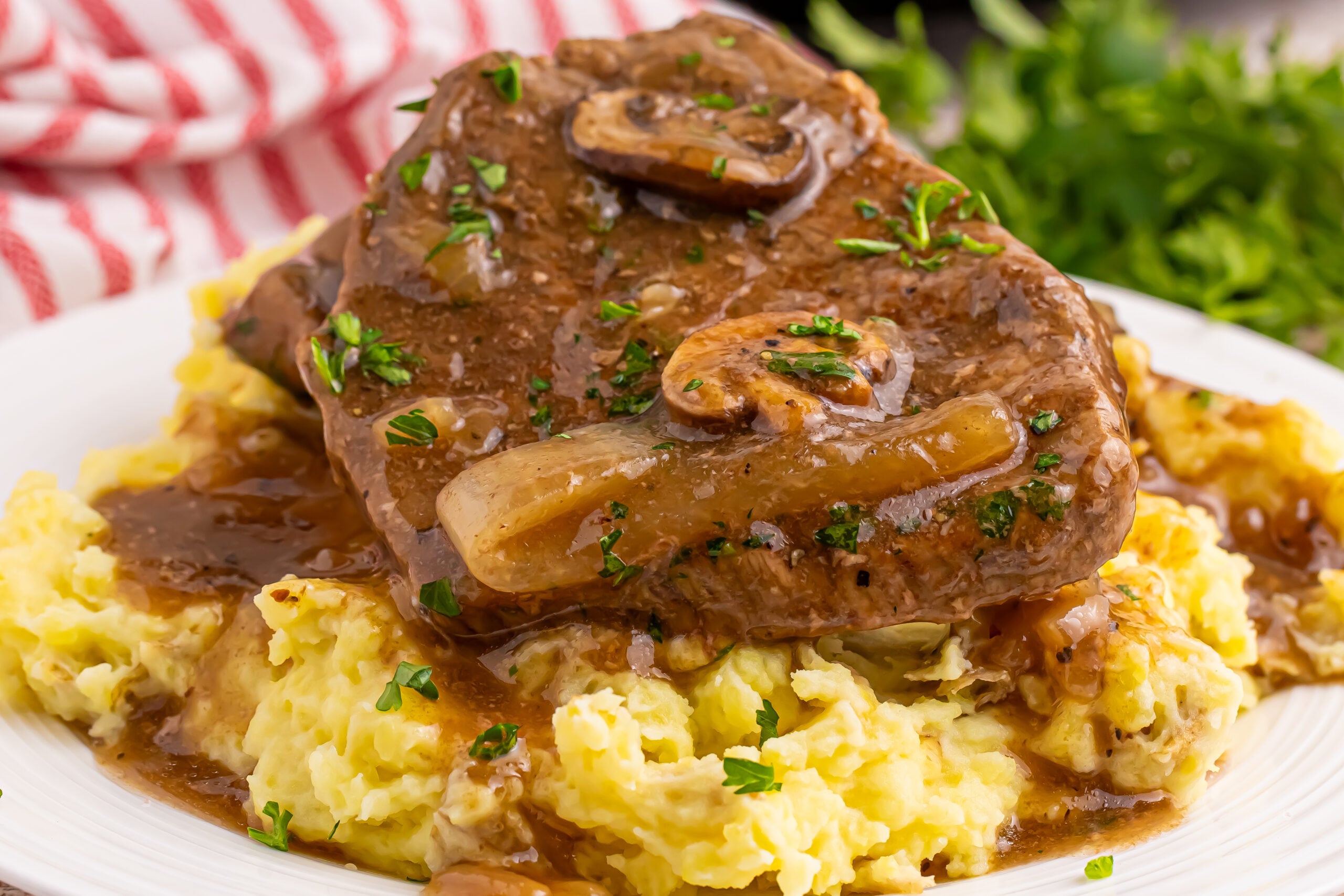 Slow Cooker Round Steak and Gravy on a plate with a bed of mashed potatoes under the steak and gravy