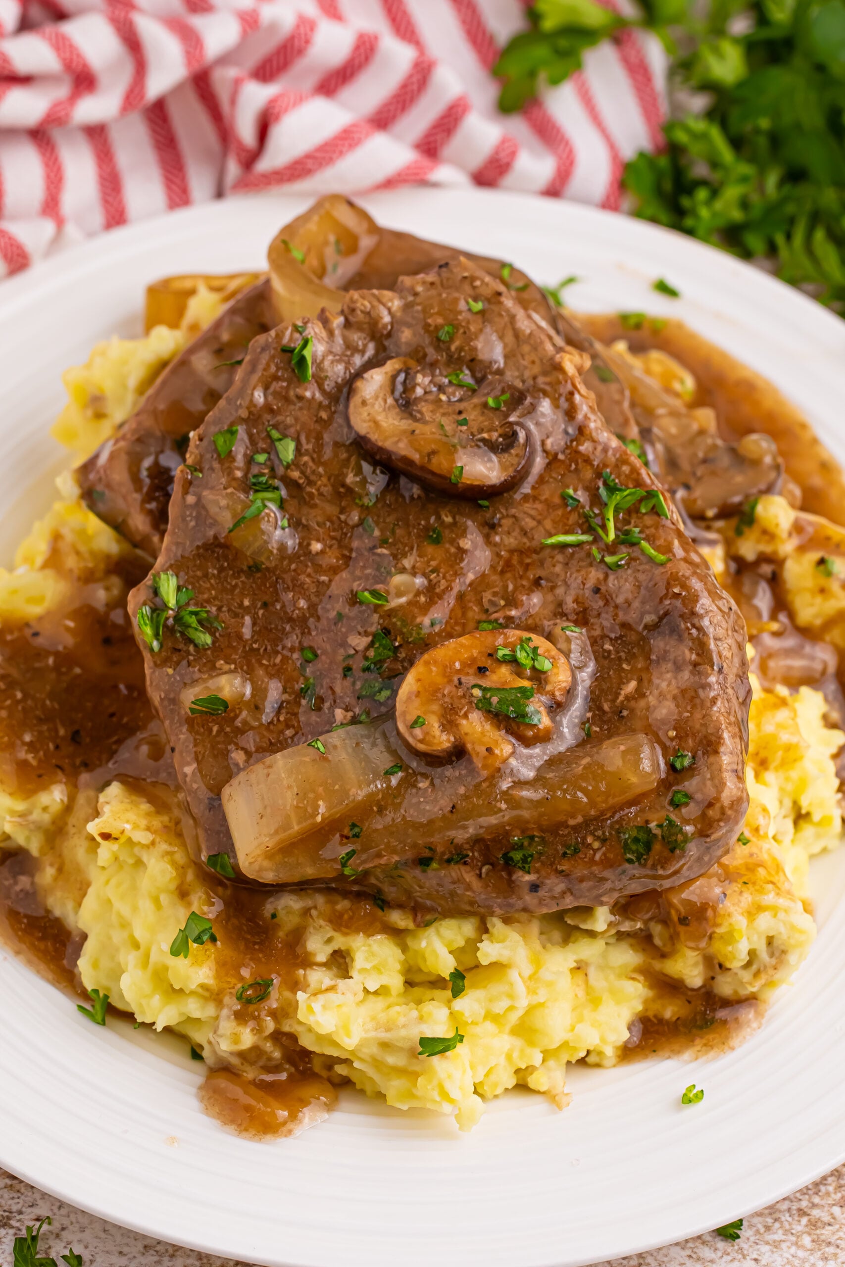plate with a spread of mashed potatoes topped with steak, onions and mushroom gravy. There is a crock pot in the background
