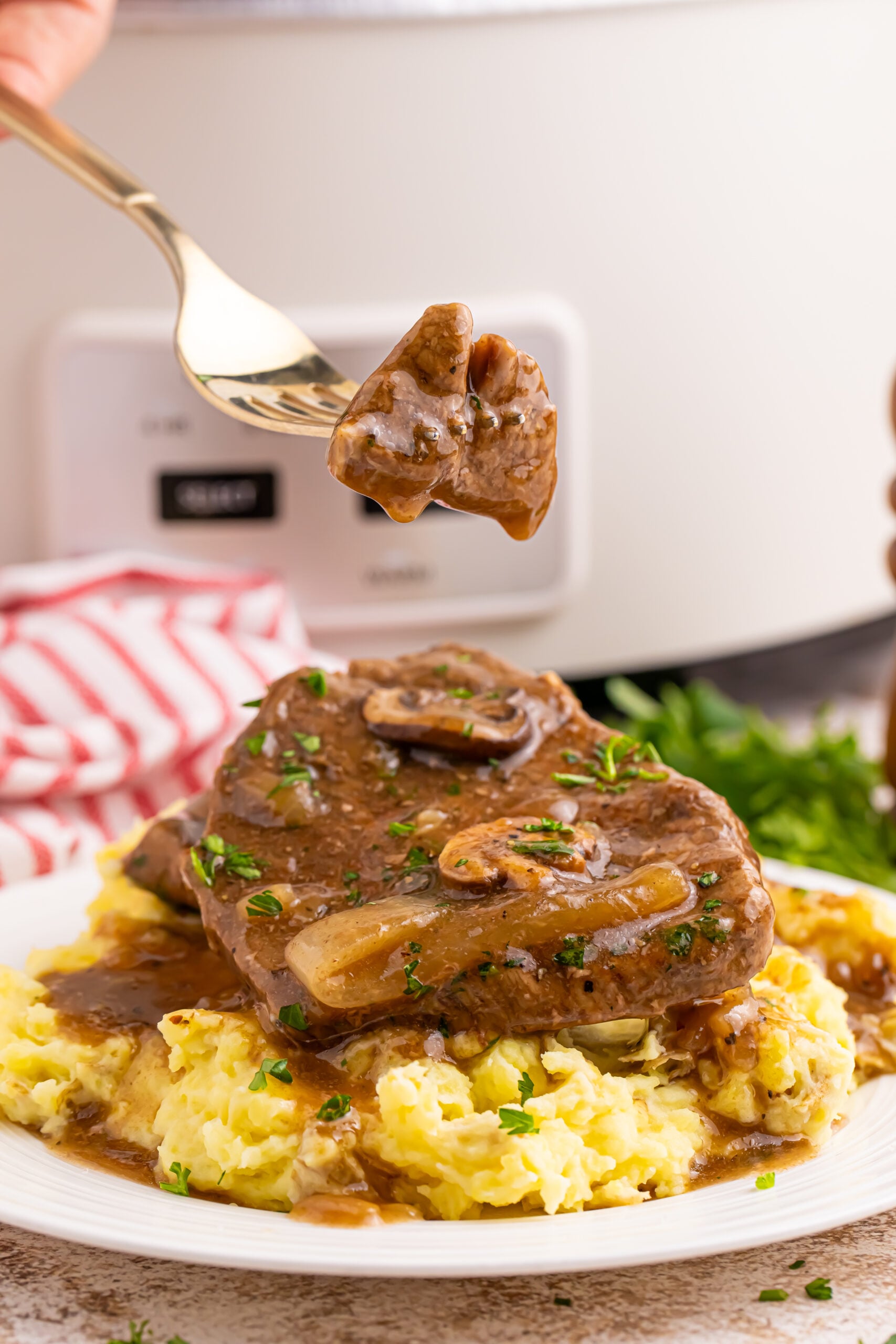steak, gravy, and potatoes on a plate with a fork with a bit of the Slow Cooker Round Steak and Gravy on it