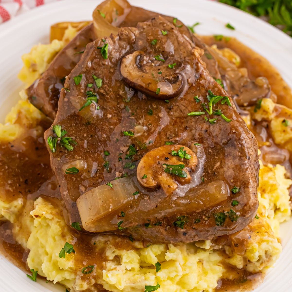 Slow Cooker Round Steak and Gravy on a plate with a bed of mashed potatoes under the steak and gravy