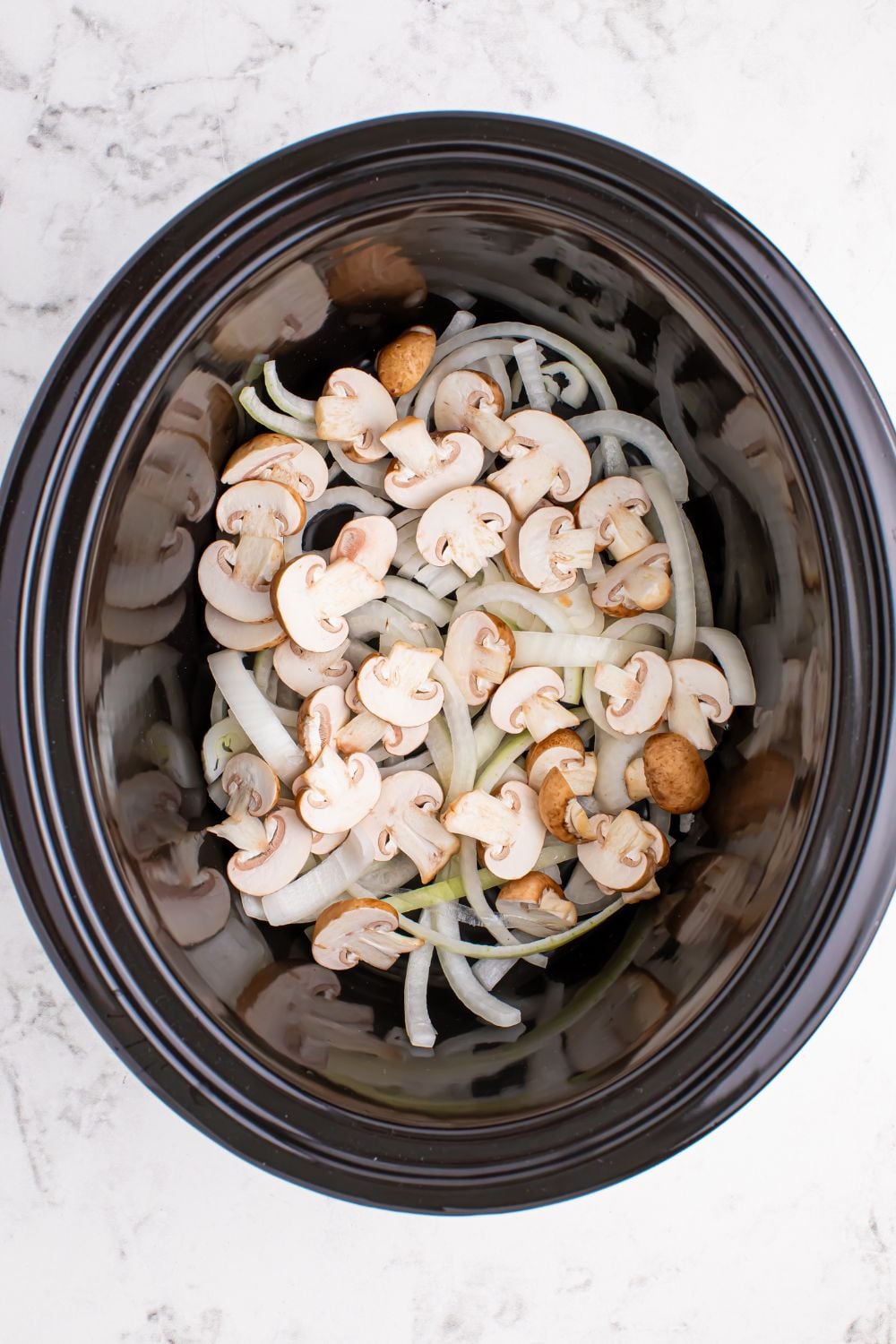 mushrooms and onions in a crockpot sitting on the table