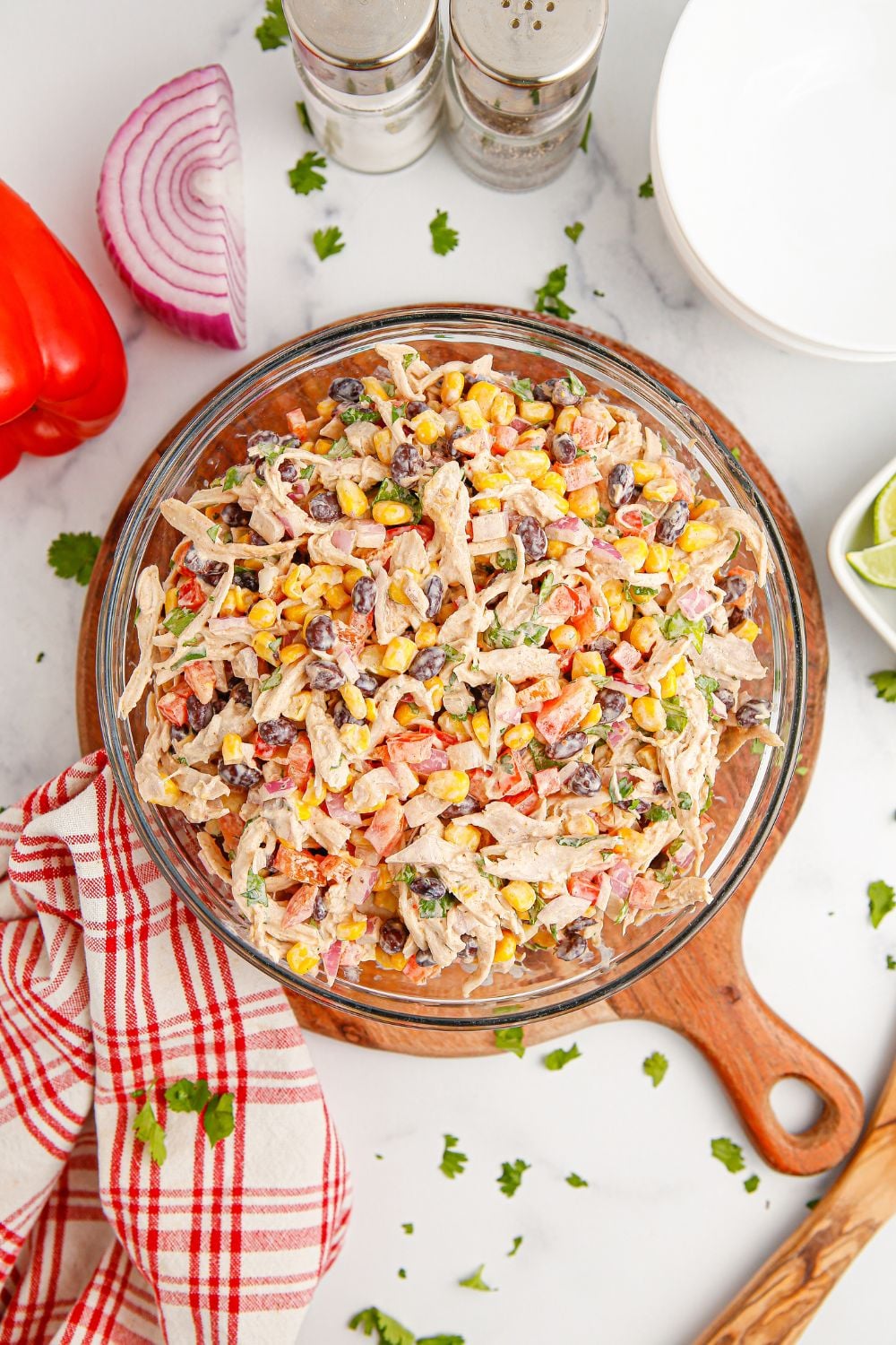 Southwest Chicken Salad in a bowl sitting on table with salt and pepper and a towel by it and vegetables