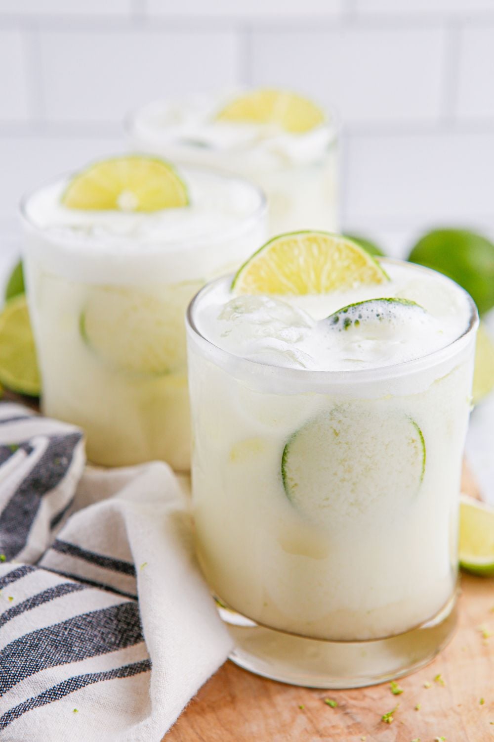 three glasses of Brazilian Limeade sitting on table with a towel and limes around it on table