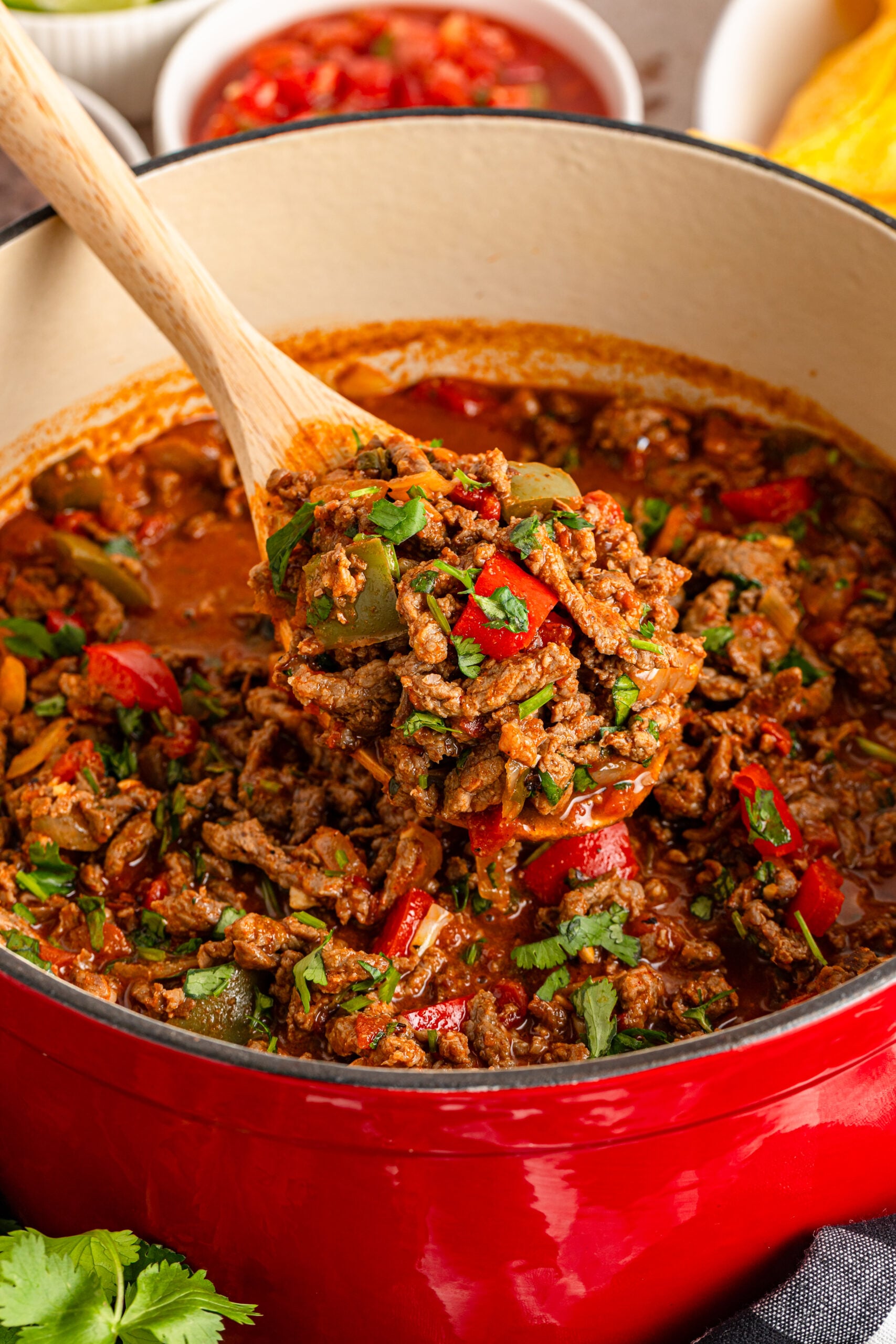 Carne Picada in a dutch oven pot with a wooden spoon lifting up some to show texture