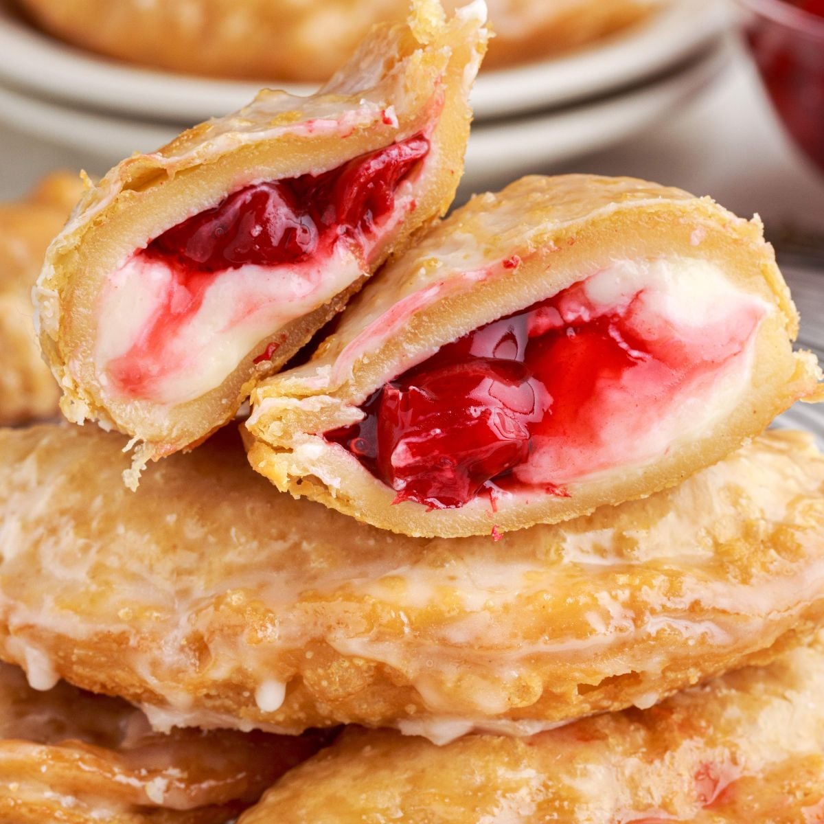 Cherry Cheesecake Hand Pies stacked on table with on cut in half to show the filling