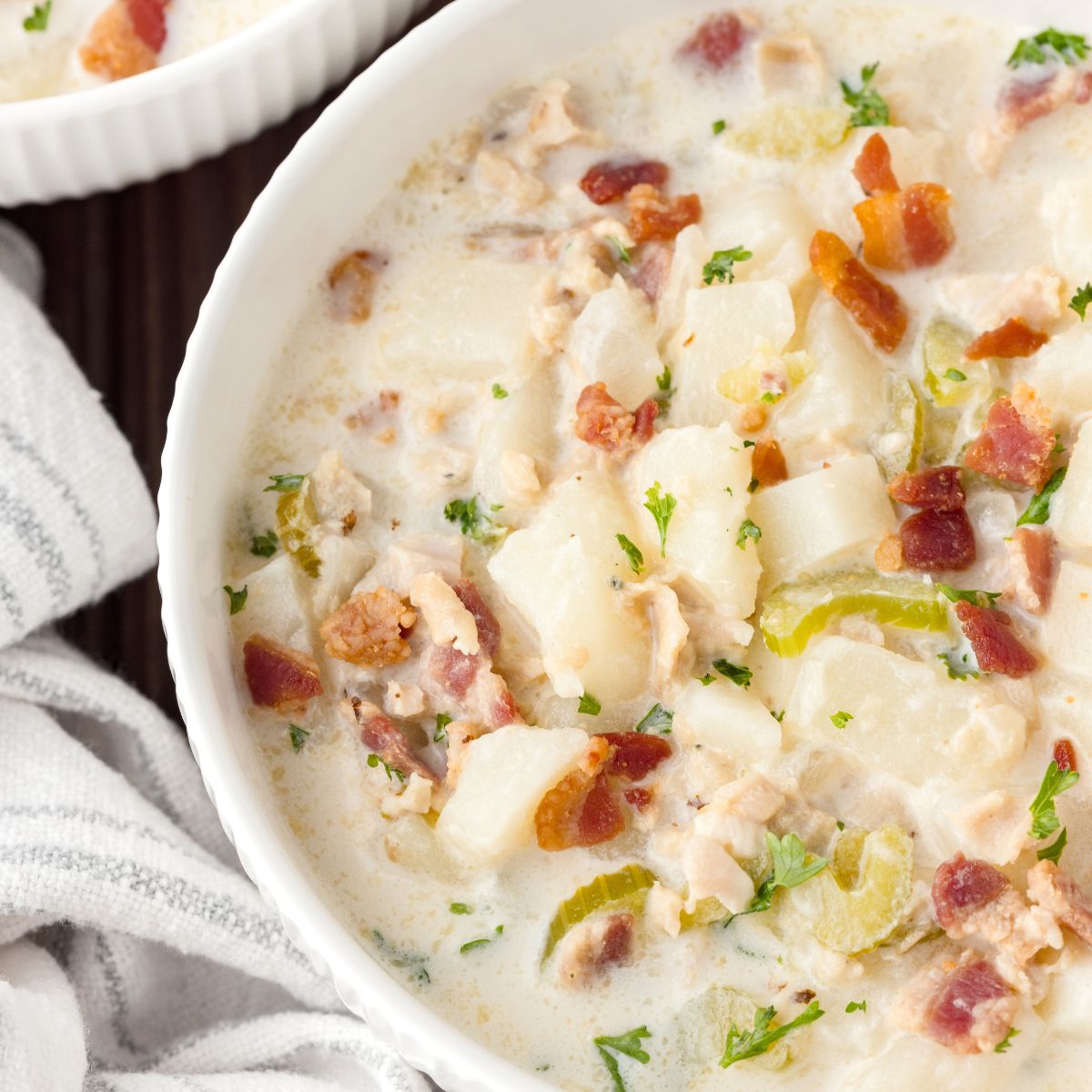 New England Clam Chowder in a bowl with a towel beside it sitting on table 