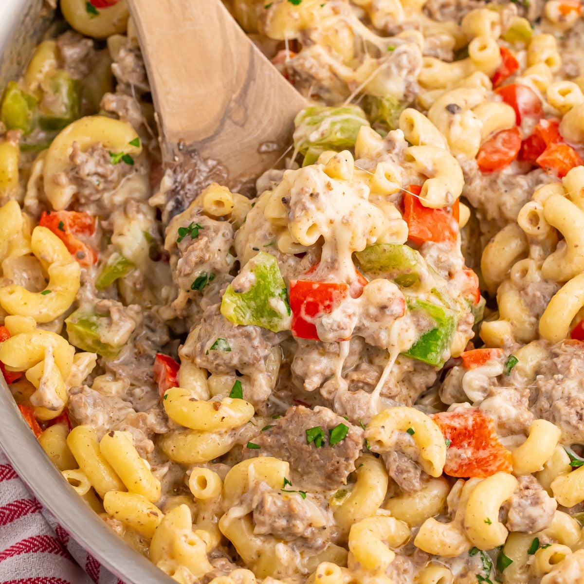 Philly Cheesesteak Pasta in a pan with a wooden spatula with some of the mixture on it 