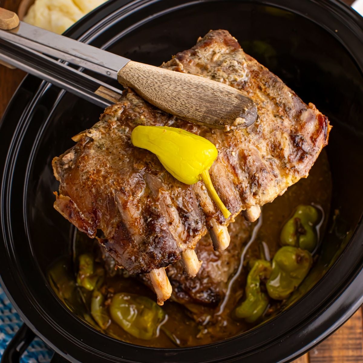 Slow Cooker Mississippi Ribs in crockpot with a rib section being lifted out of crockpot with tongs