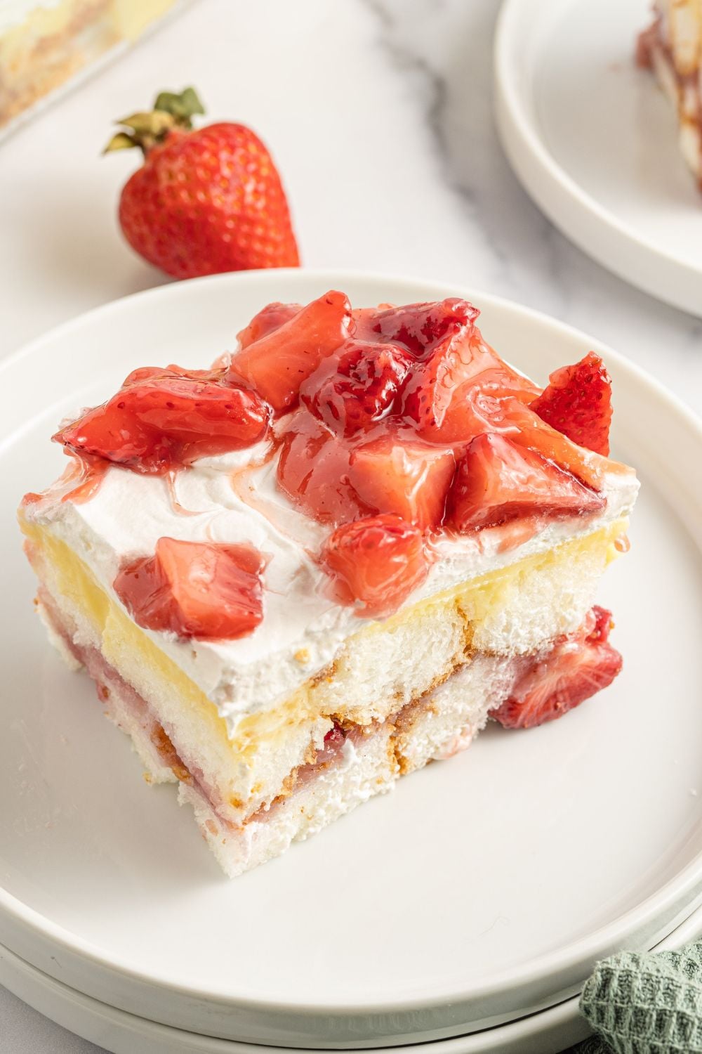 slice of strawberry heaven on earth cake on ap late with a strawberry on table behind it