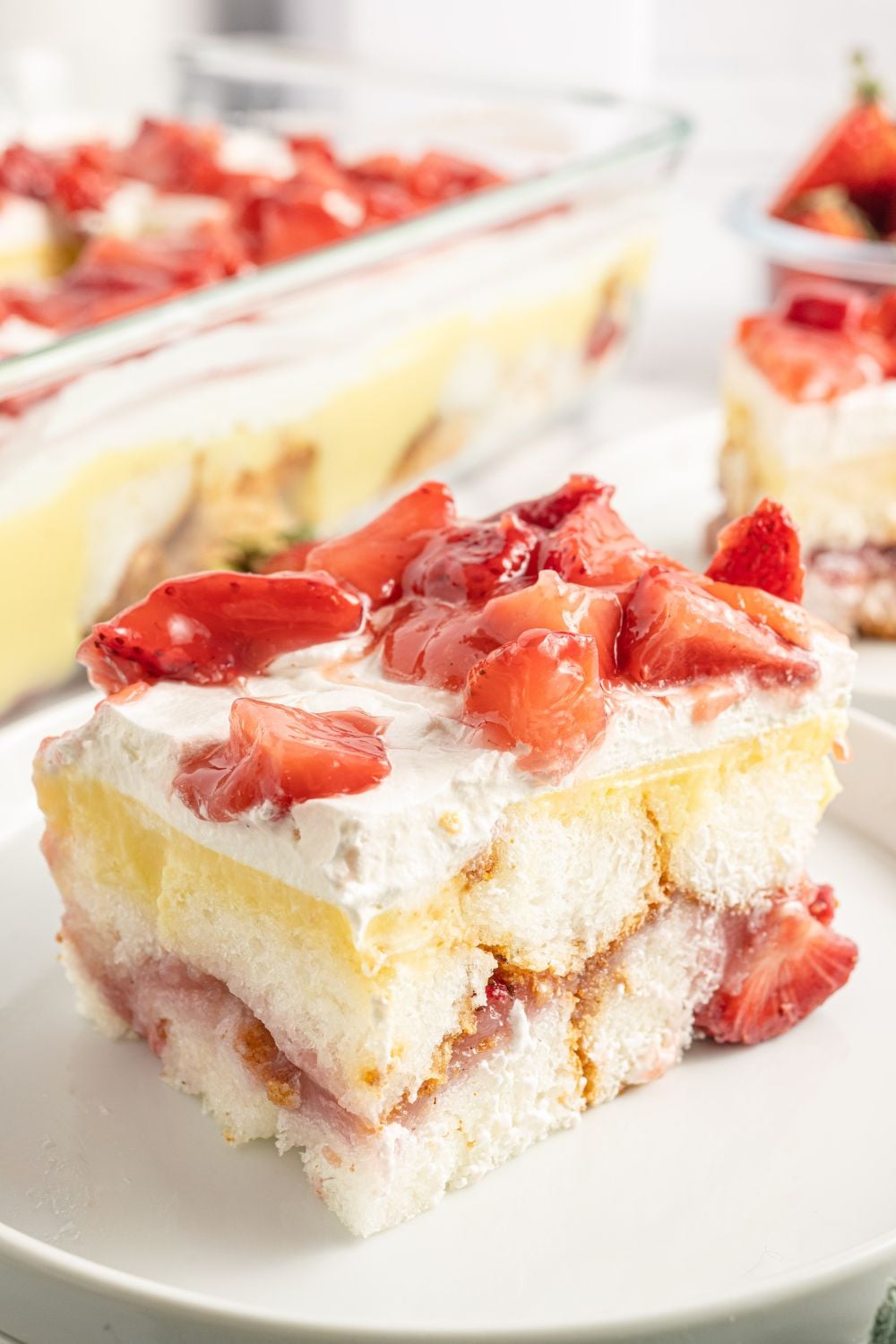 Strawberry Heaven On Earth Cake in a pan in background with a plate and a slice of the cake on it to showcase the layers of ingredients